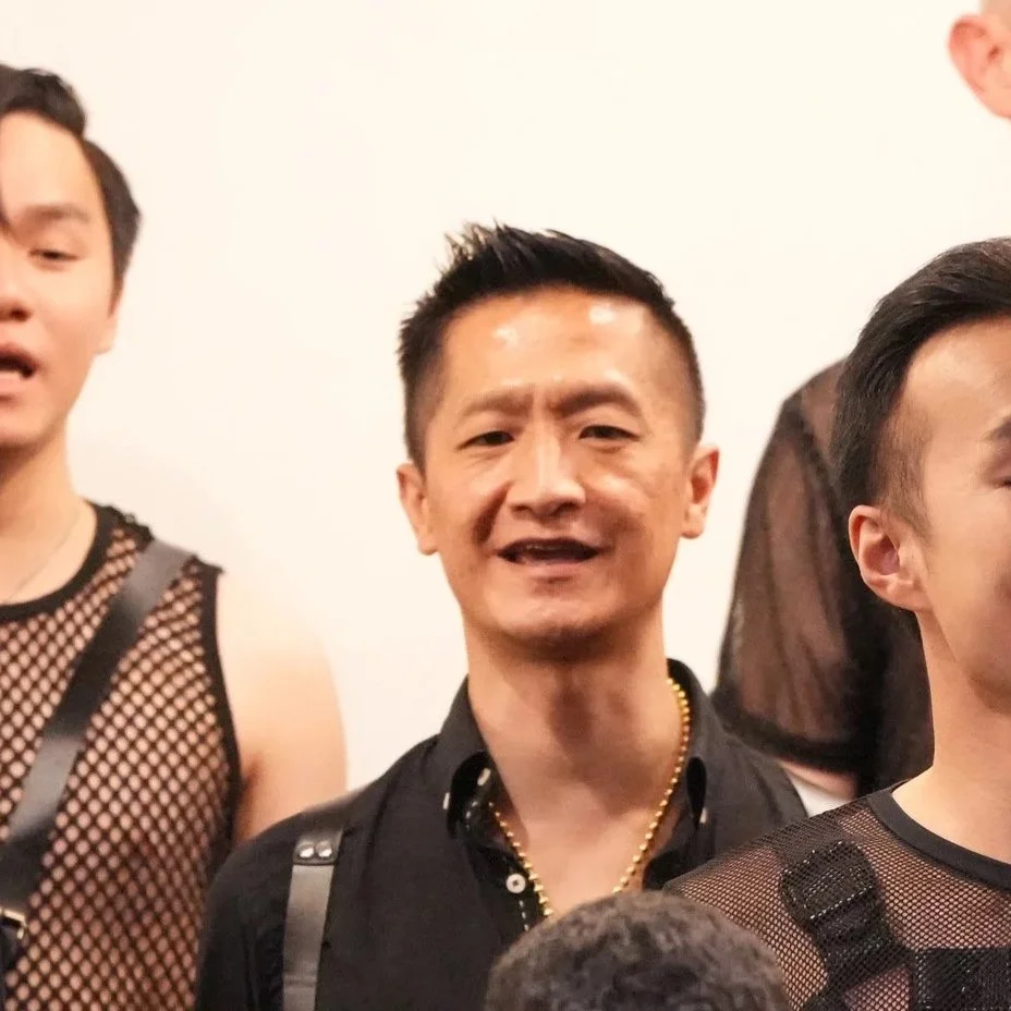 Group of men at a social gathering, wearing mesh and black shirts, with one smiling at the camera.
