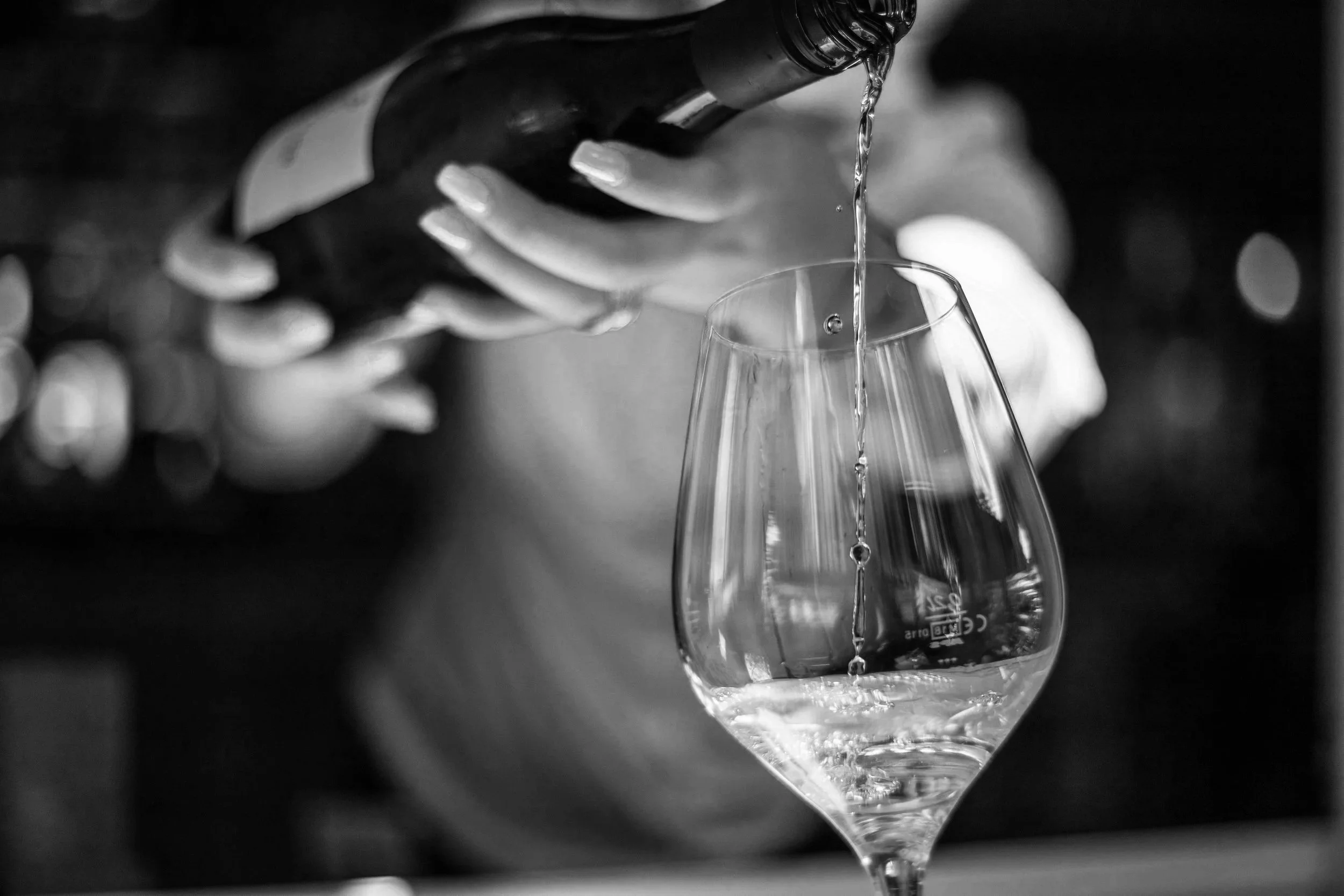 A person pouring water into a wine glass in black and white.