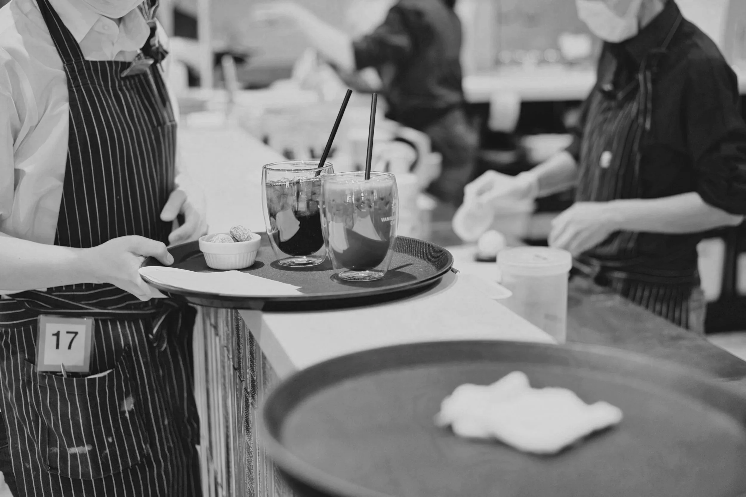 Waitstaff serving drinks with straws on a tray at a restaurant.