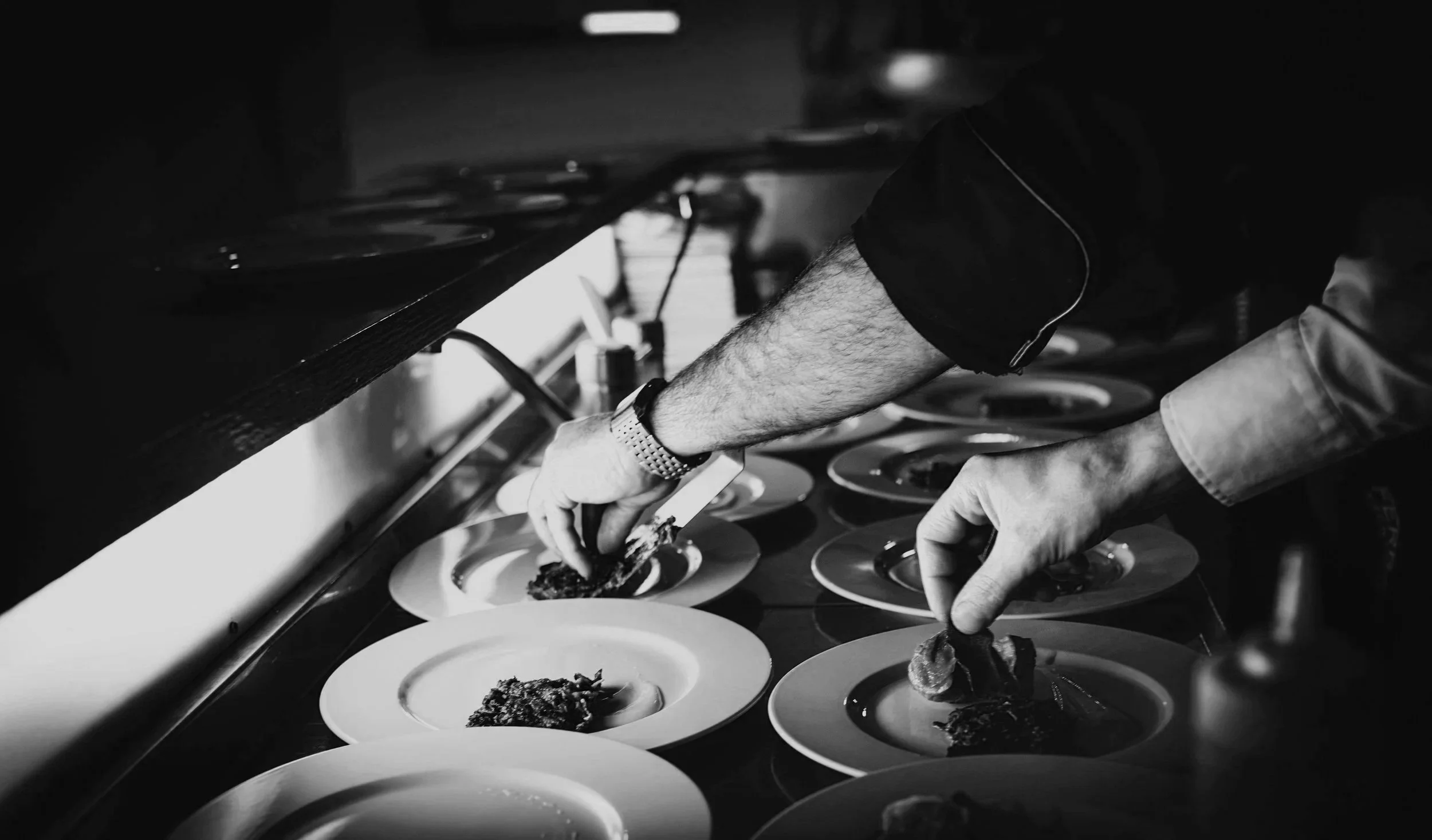 A chef plating dishes in a professional kitchen, using tweezers to carefully arrange food on plates.