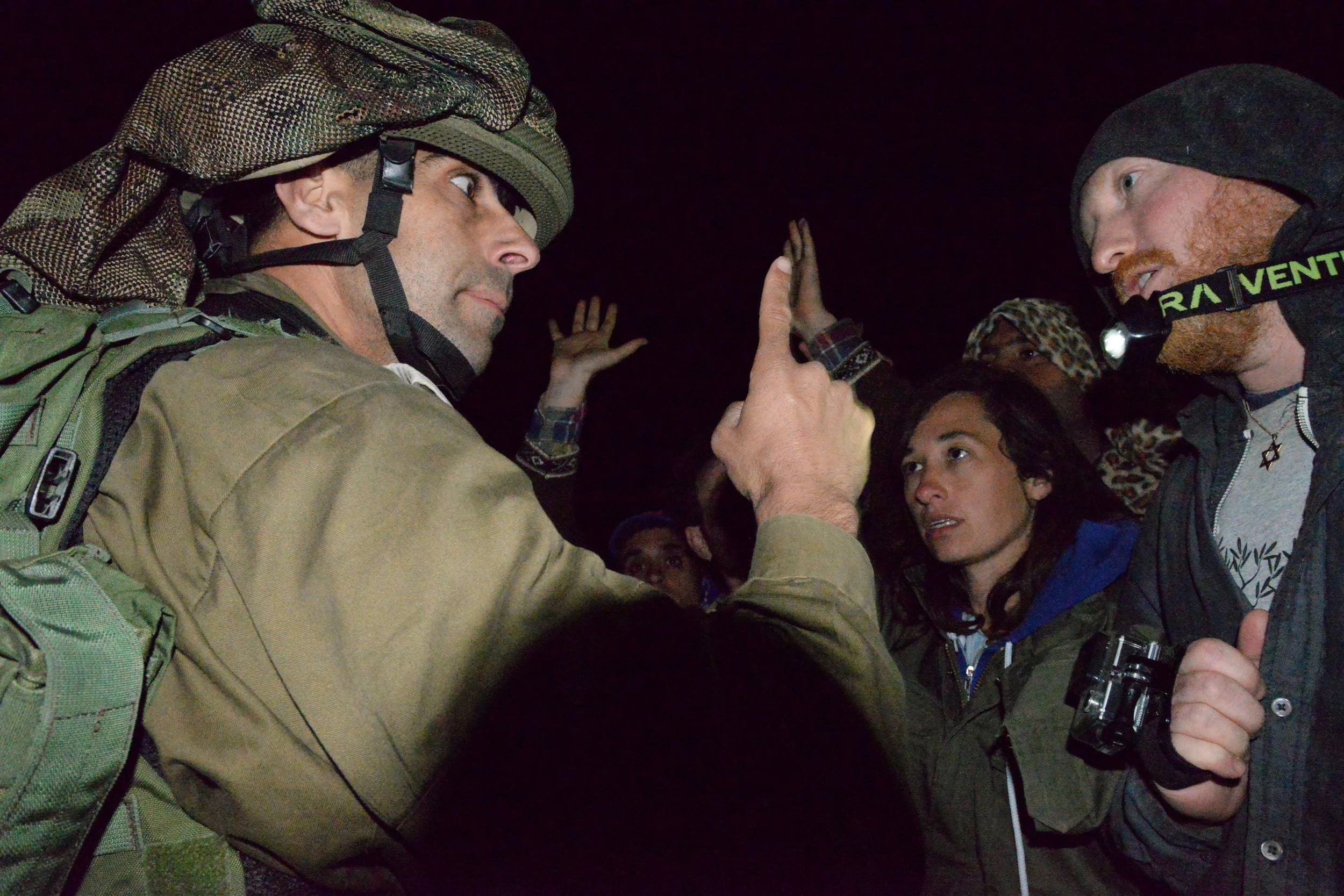 Two men wearing headlamps and outdoor gear high-fiving each other at night, with several people in the background.