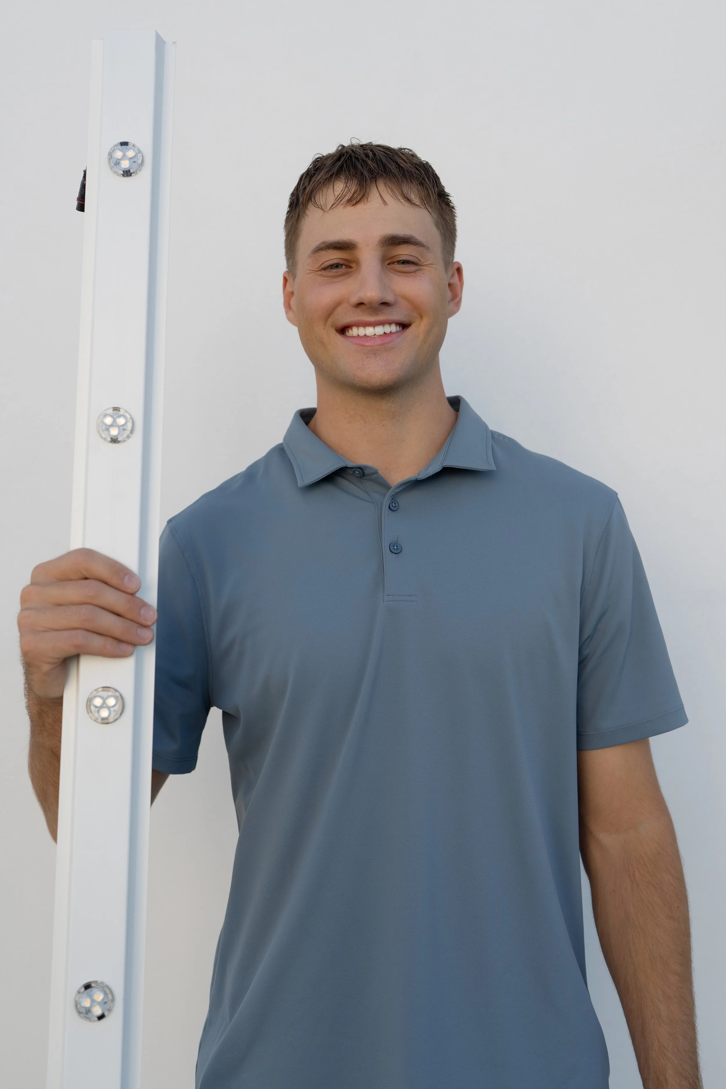 Portrait of young man smiling and holding a leveling tool against a plain white background.