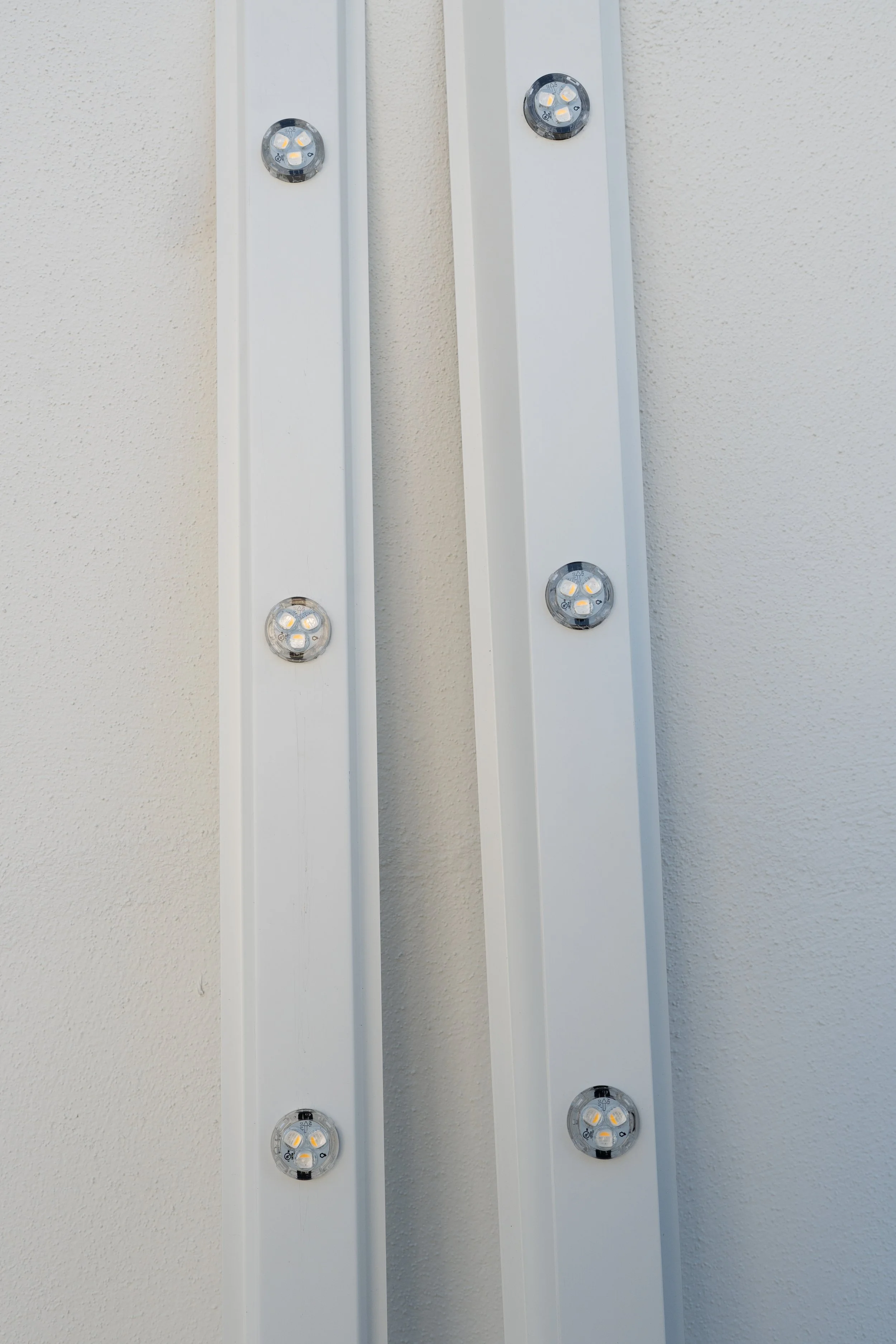 Two vertical white LED light fixtures mounted on a beige wall.
