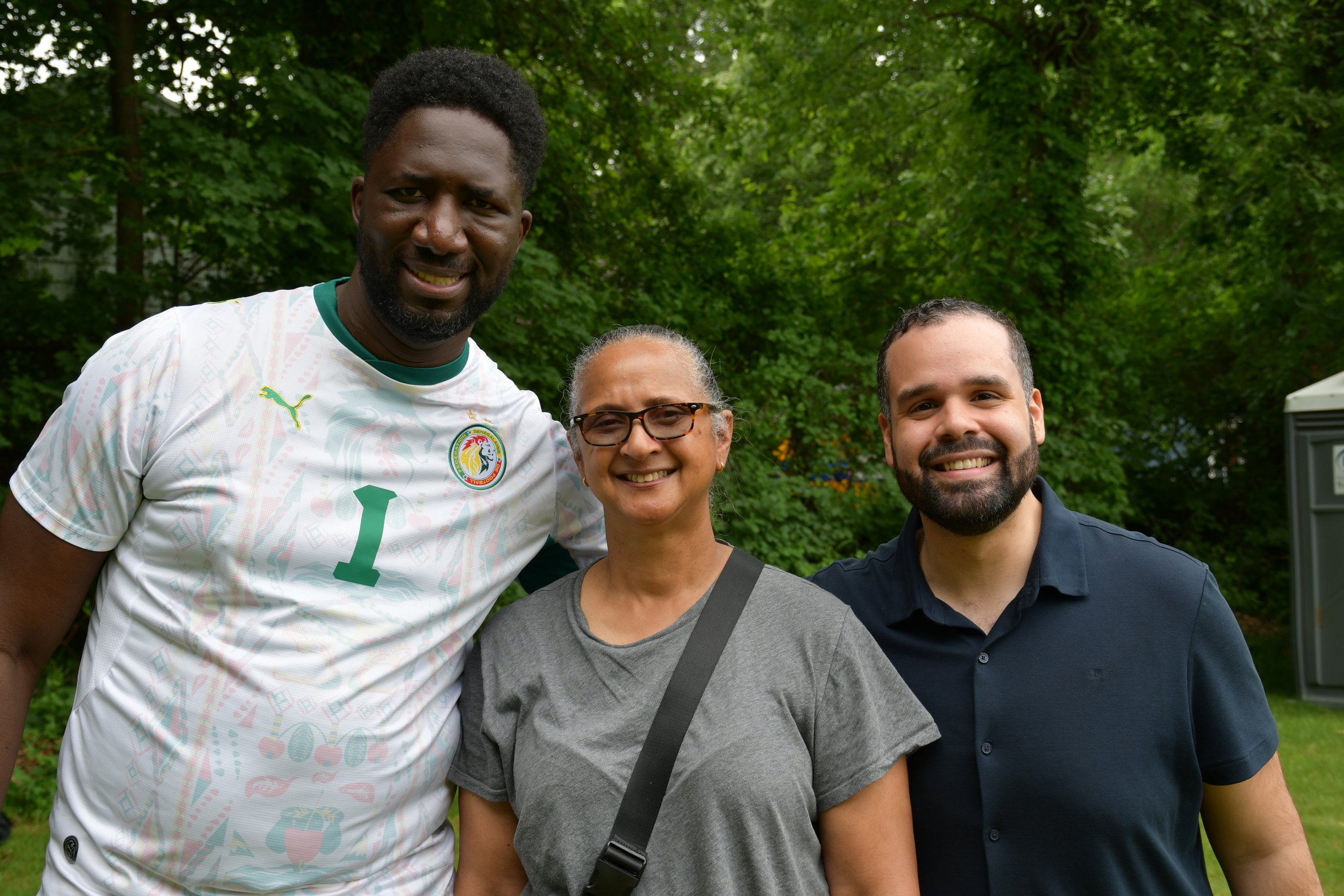 Three people, two men and one woman, smiling outdoors with trees in the background.