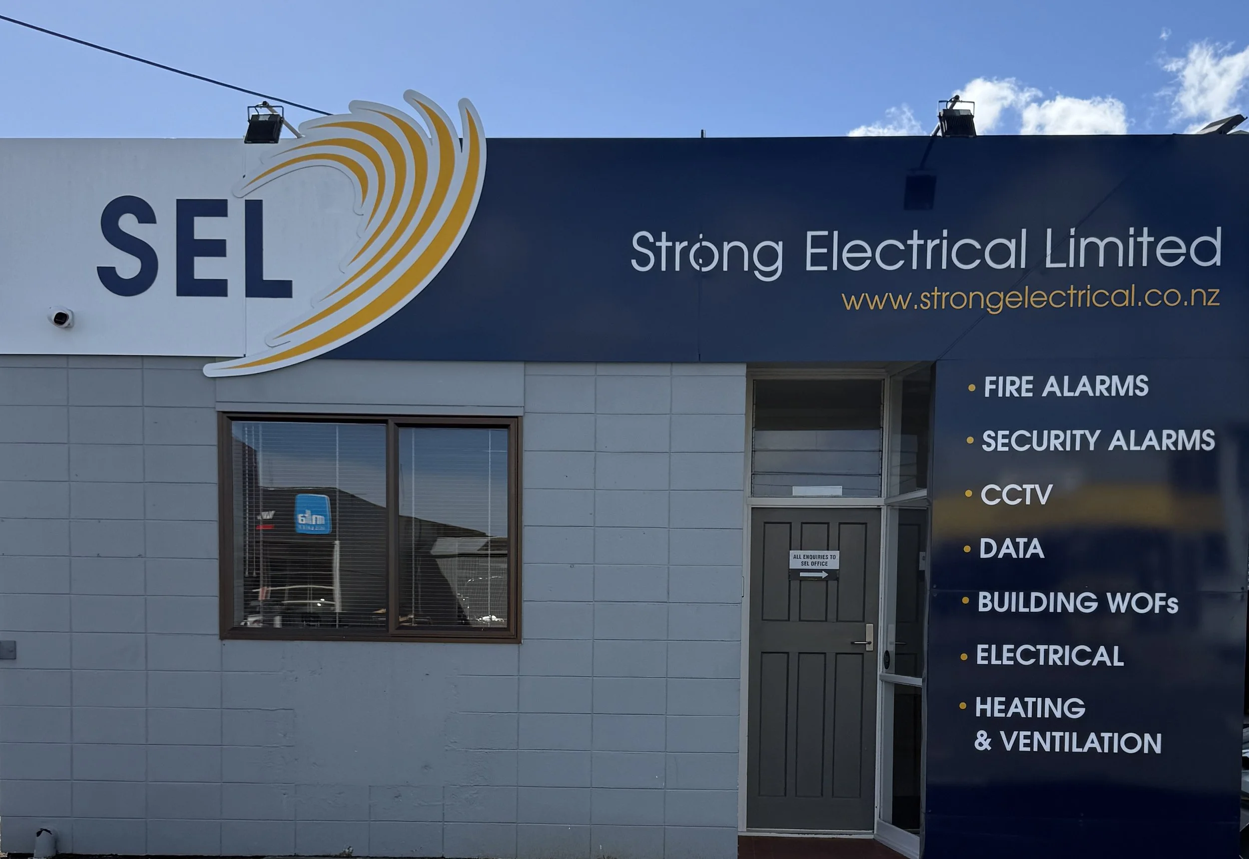 Sign for Strong Electrical Limited displaying services like fire alarms, security alarms, CCTV, data, building WOFs, electrical, heating, and ventilation, with a logo resembling a yellow wave.
