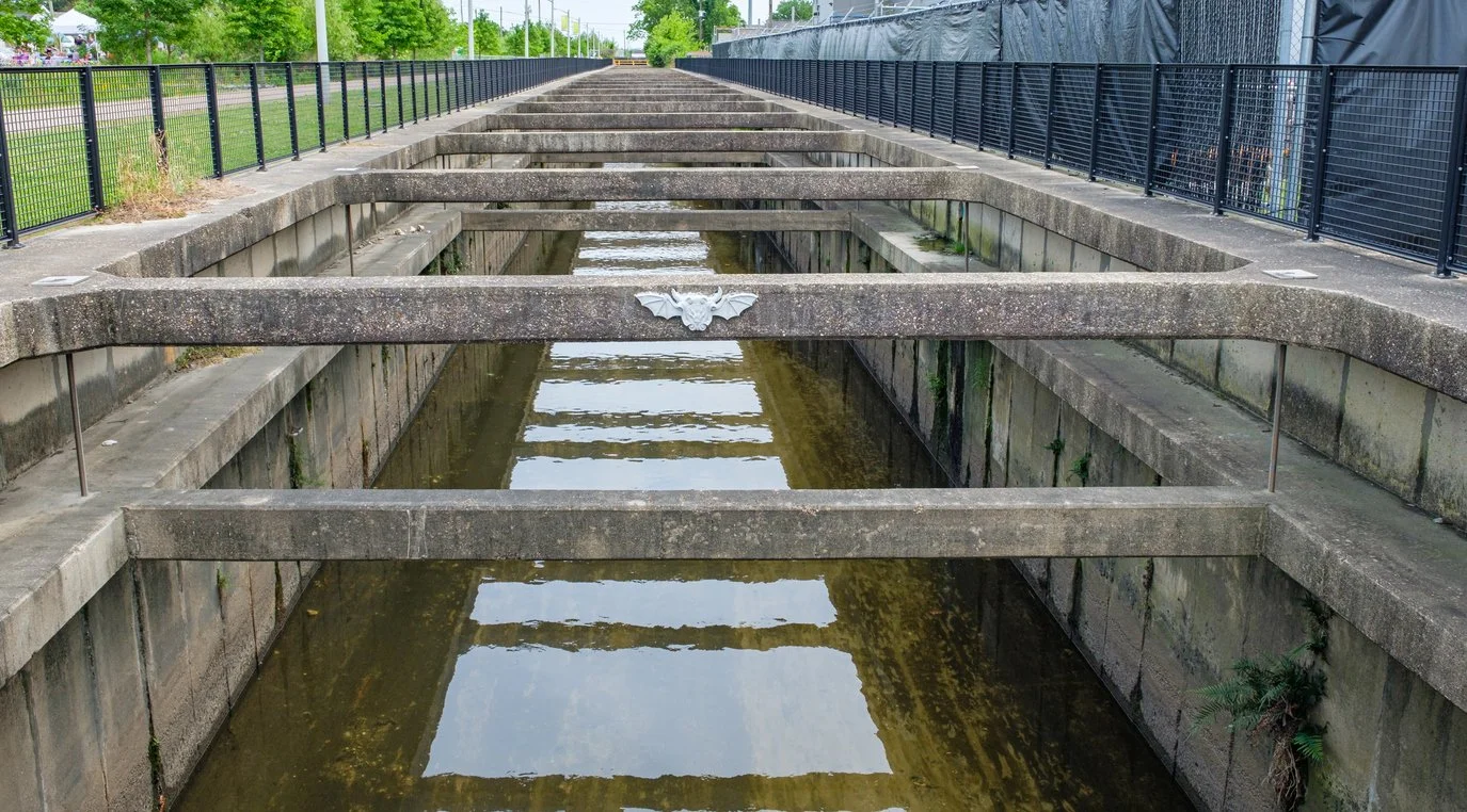 Empty waterway with concrete sides, horizontal concrete beams, and black metal fencing on both sides.