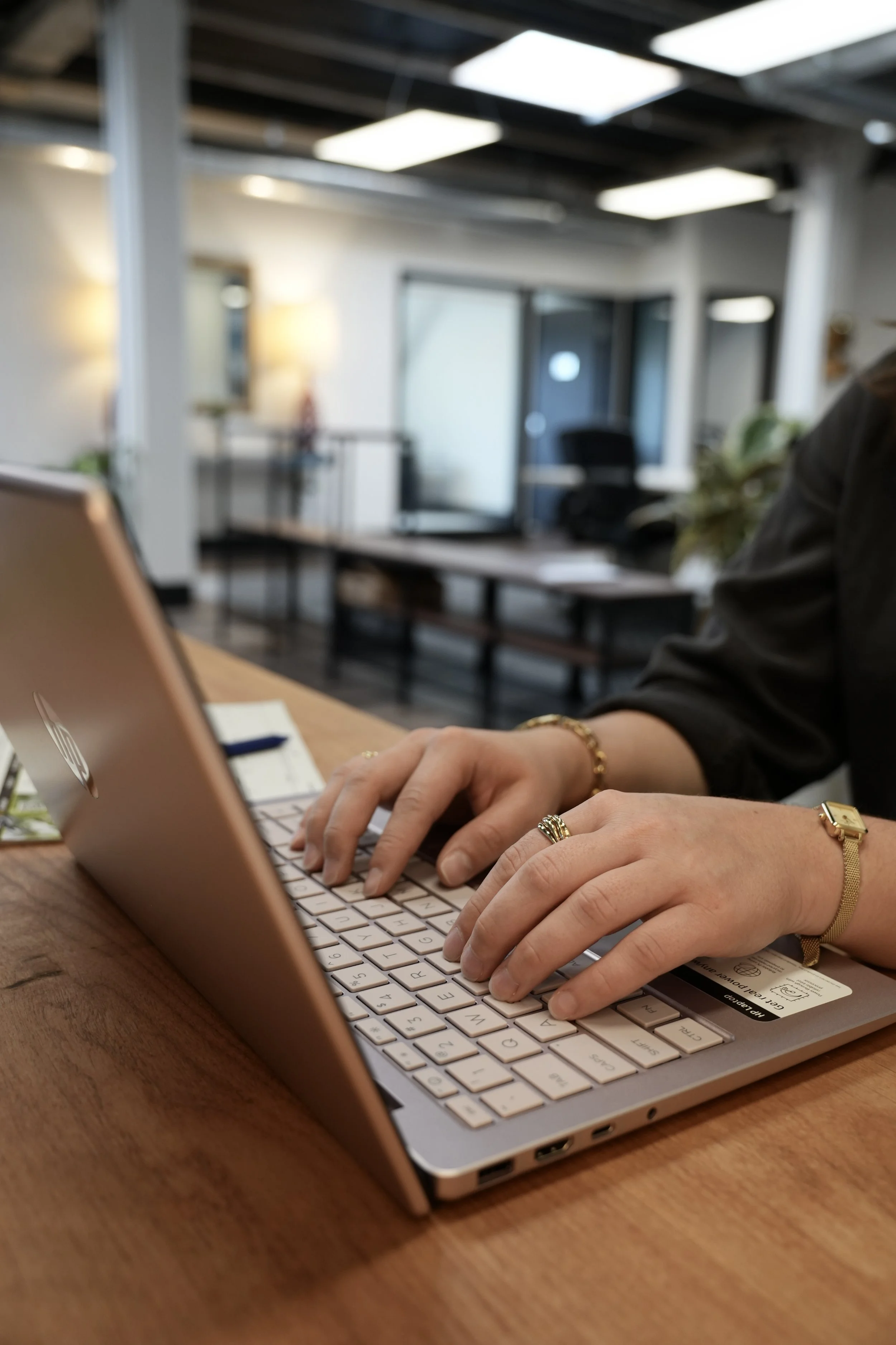 Person typing on a laptop at a wooden desk in a modern office