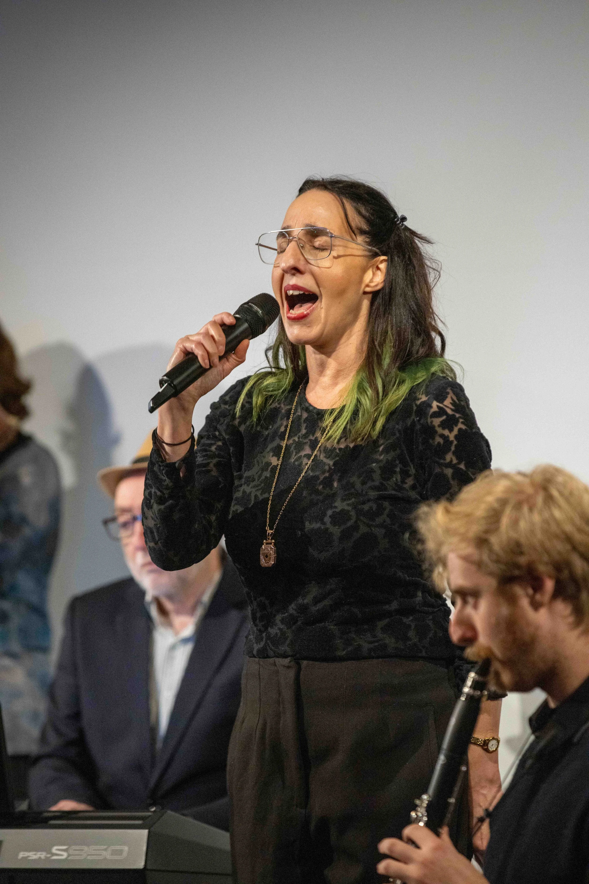 A woman singing passionately into a microphone during a live performance or event, with people seated around her.