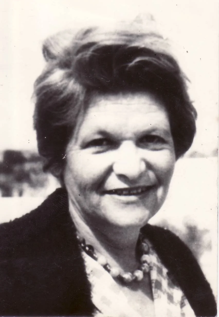 Black and white photograph of a smiling woman with short, wavy hair, wearing a necklace and a dark top.