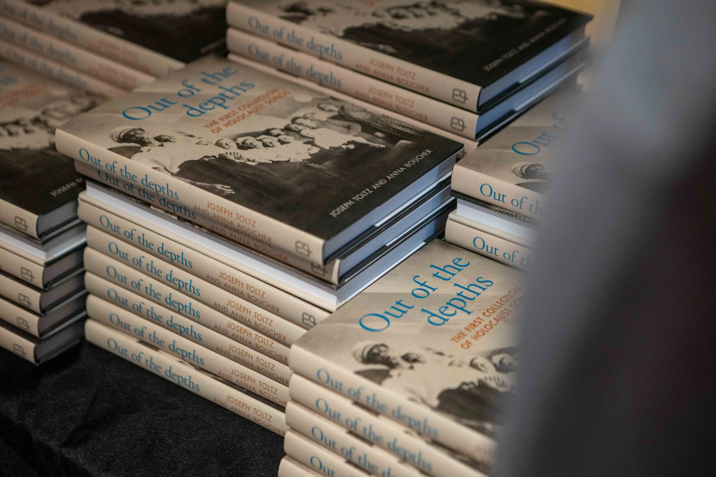 Multiple copies of the book titled 'Out of the depths' by Joseph Toitz and Anna Boucher are stacked on a dark surface.