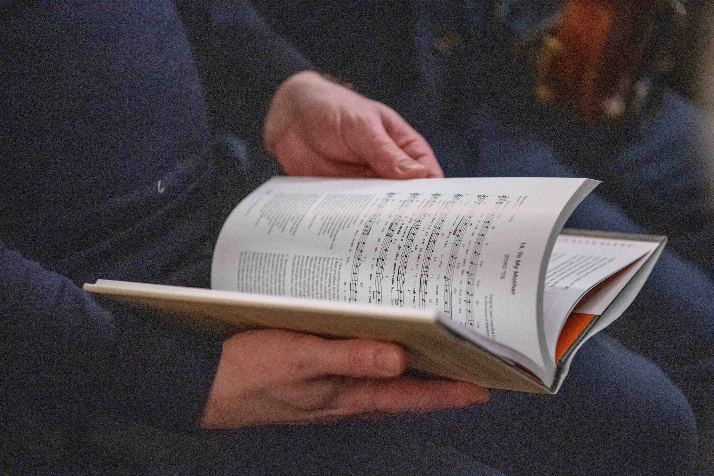 A person holding and reading a sheet of music with lyrics and musical notes.