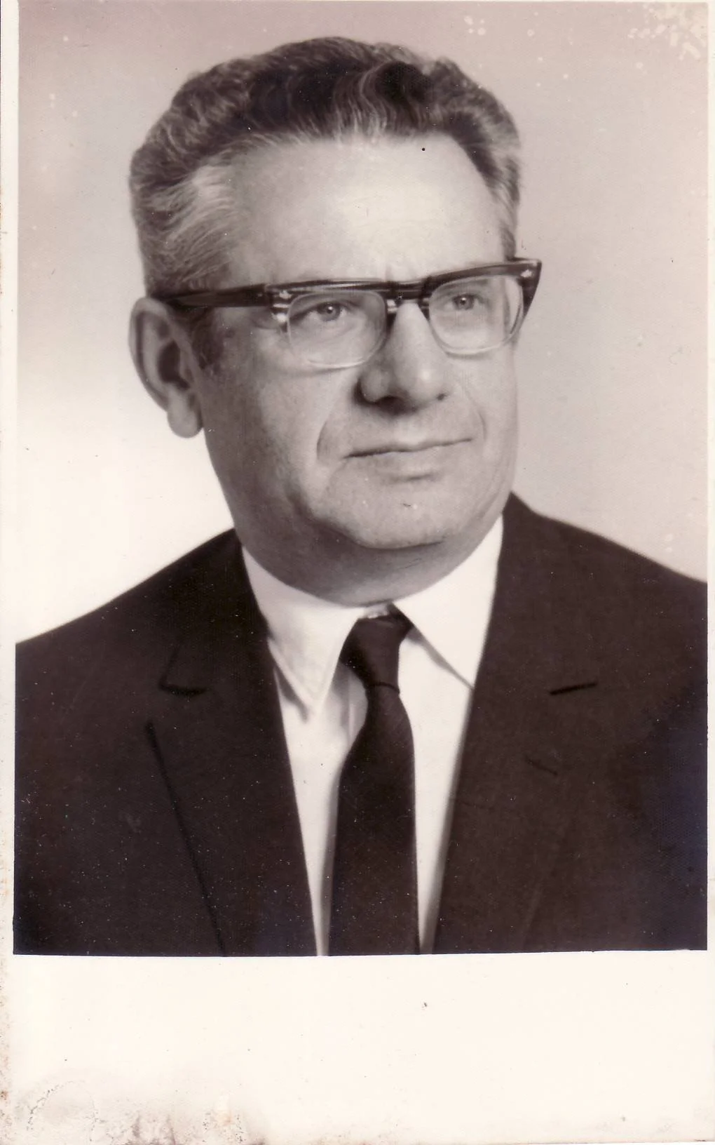 Black and white portrait of a man in a suit, tie, and glasses.