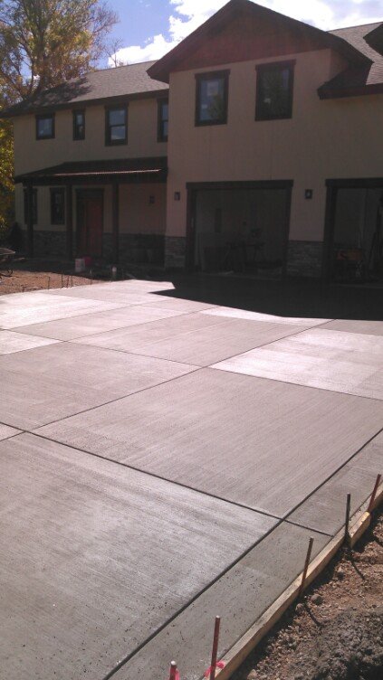 Newly poured concrete driveway in front of a two-story house with garage doors and windows.