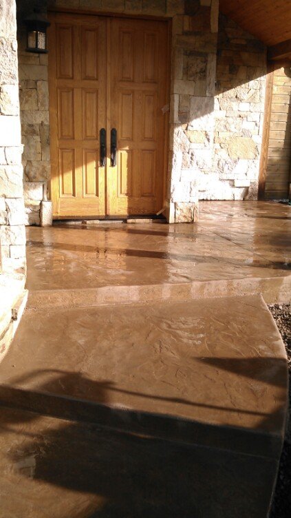 Wooden front door with black handles, stone exterior walls, and a wet concrete porch.