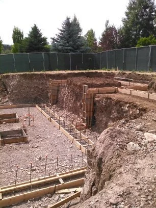 Construction site with foundation work and rebar in place, surrounded by dirt and excavation.