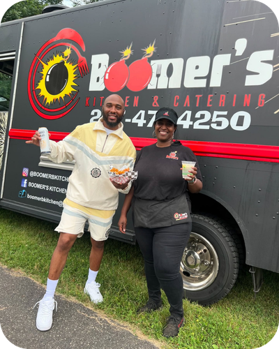 Boomer and Neef Buck standing in front of a food truck with the name 'Boomer's Kitchen & Catering.'