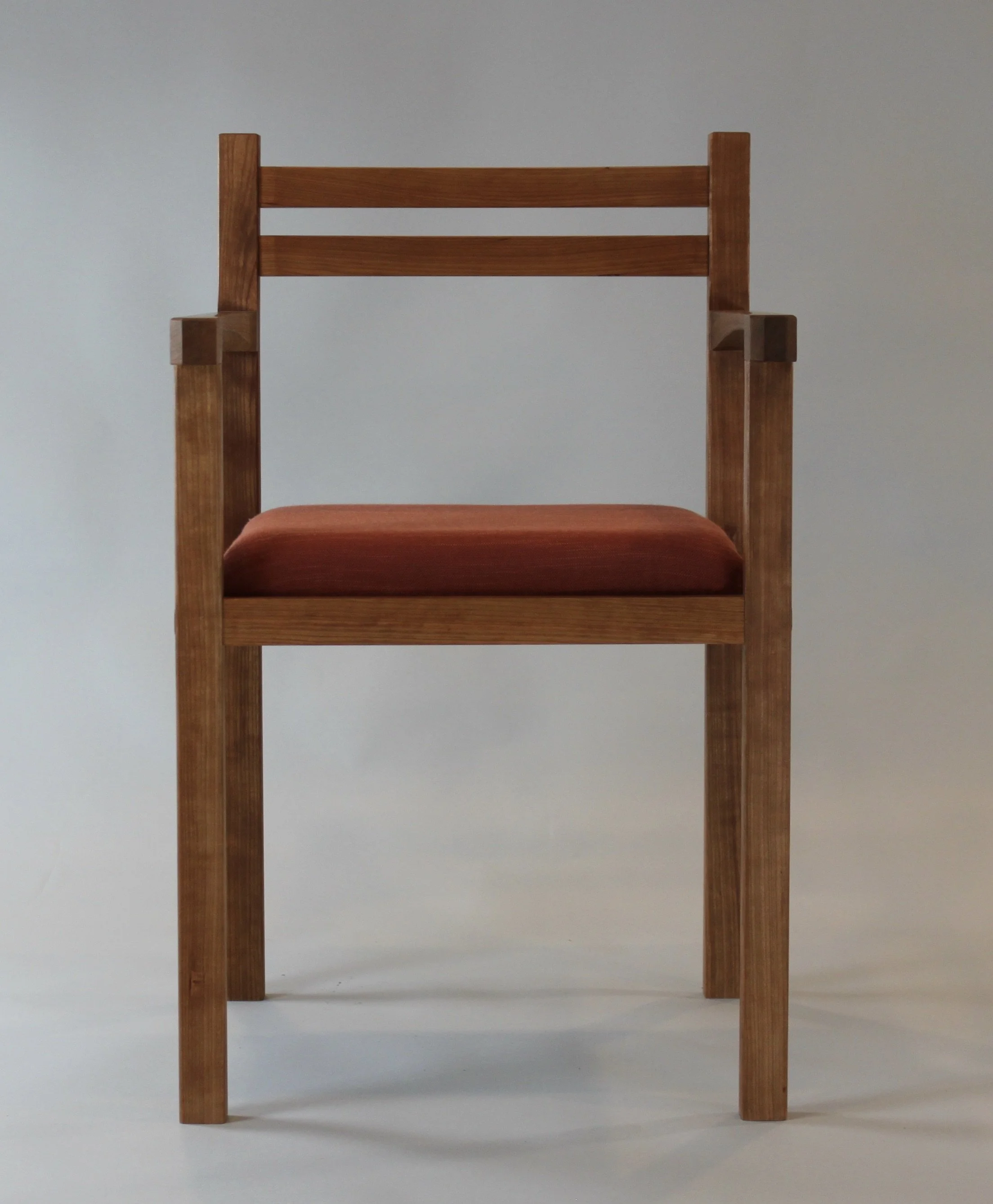 Wooden chair with a reddish-brown cushion placed on a white surface against a neutral gray background.