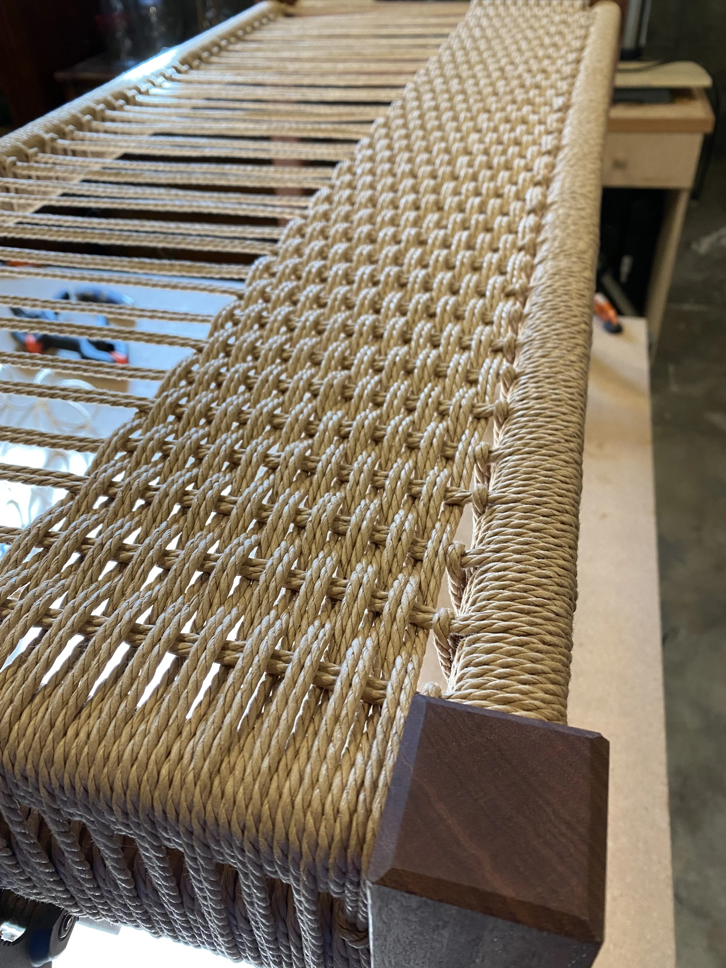 Close-up of a woven rattan or wicker bench with a wooden armrest and base.