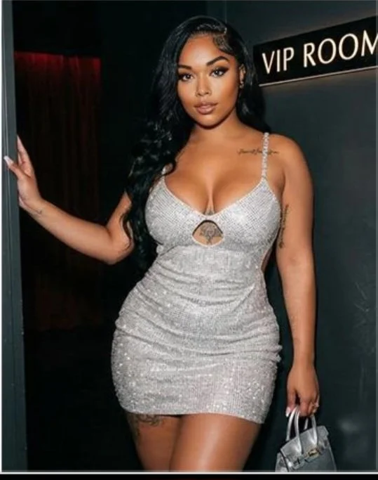 Woman in a silver, sparkly dress standing near a VIP room sign, holding a small handbag.