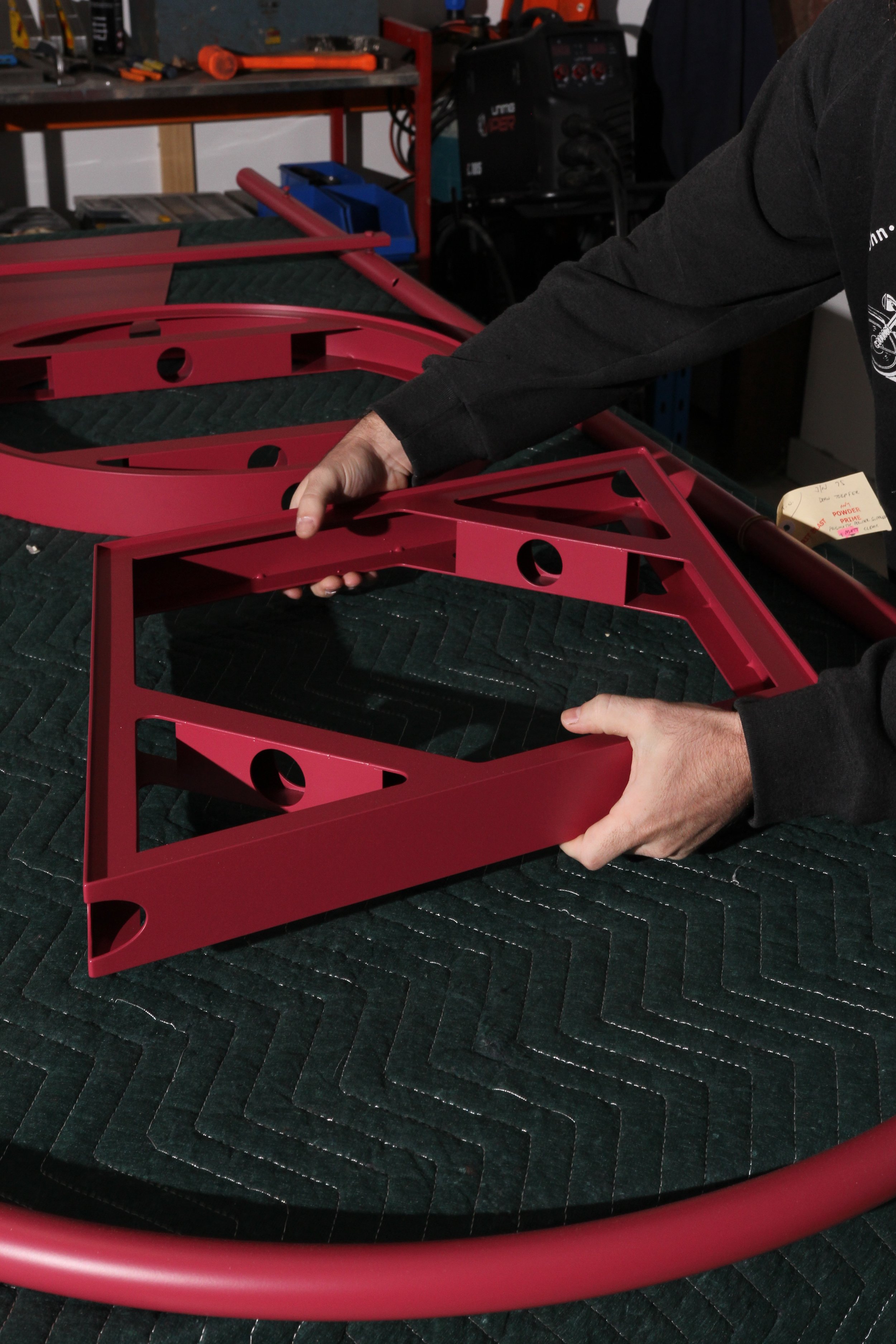 Person assembling red metal frames in a workshop with tools and equipment in the background.