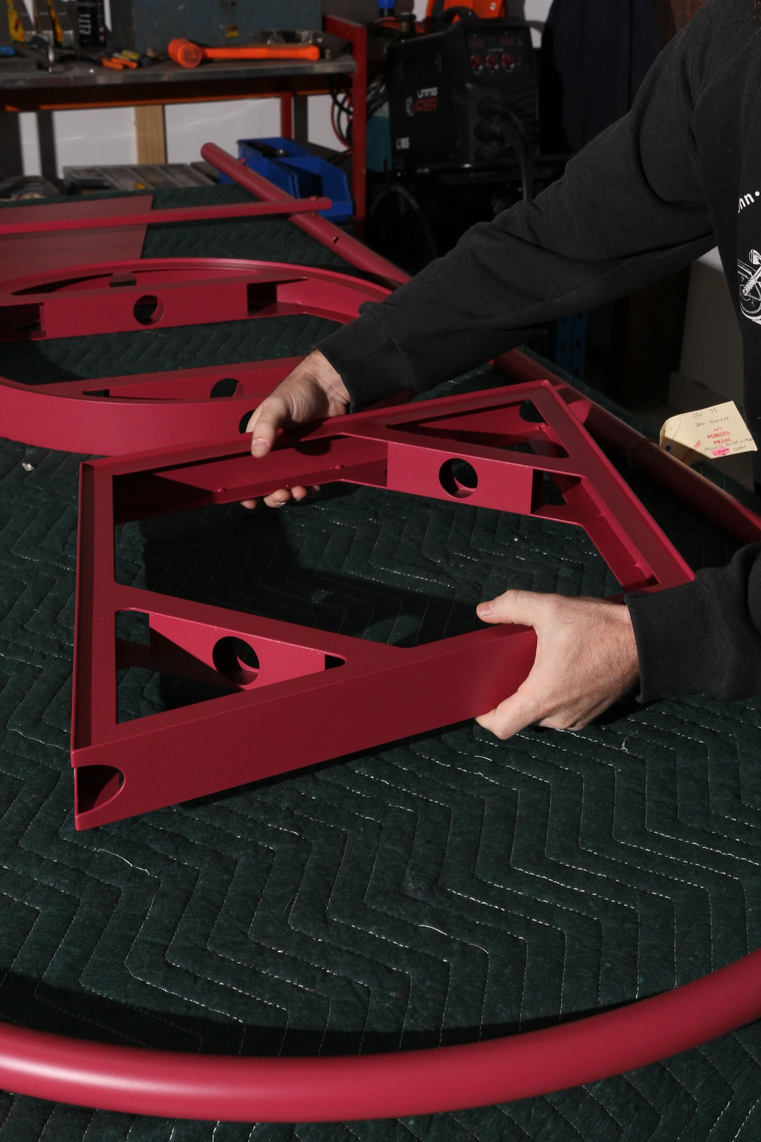 Person holding red metal frame in workshop with tools and equipment in background.