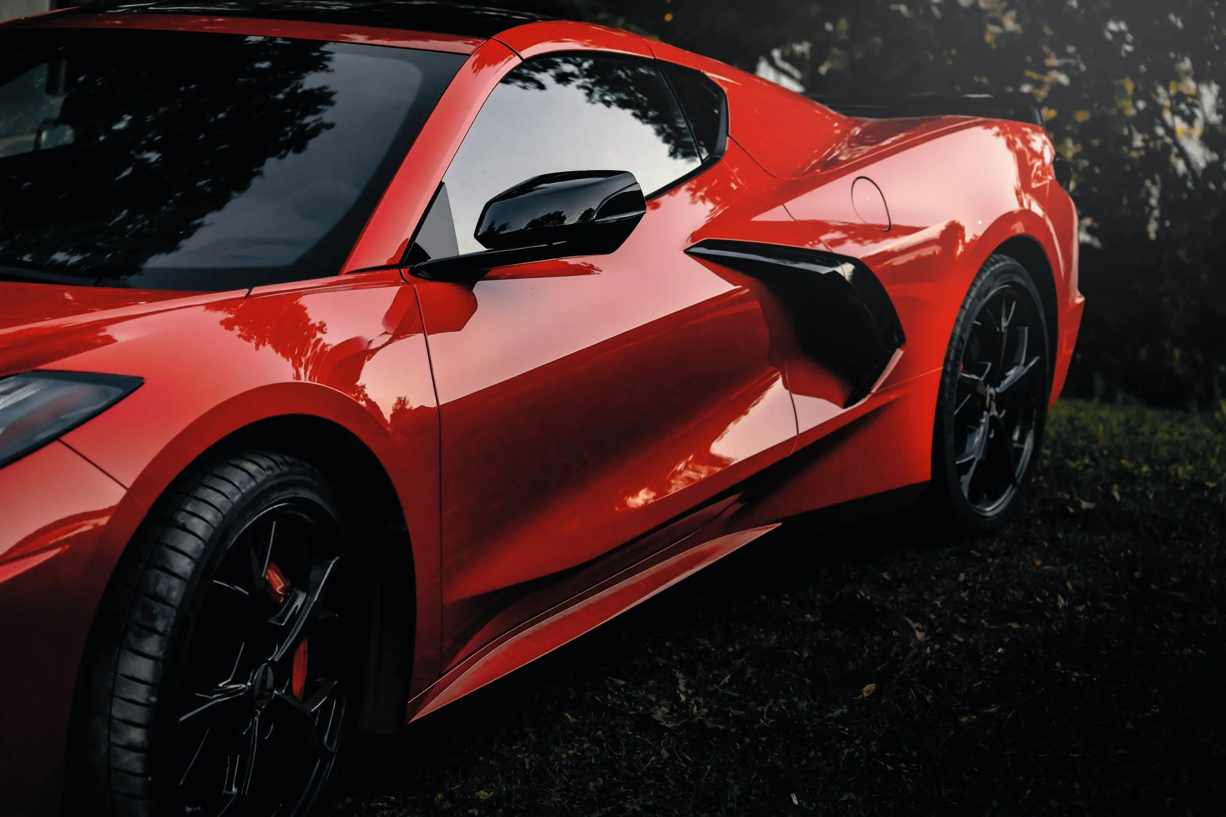 Red sports car parked outdoors with trees reflecting on its surface.