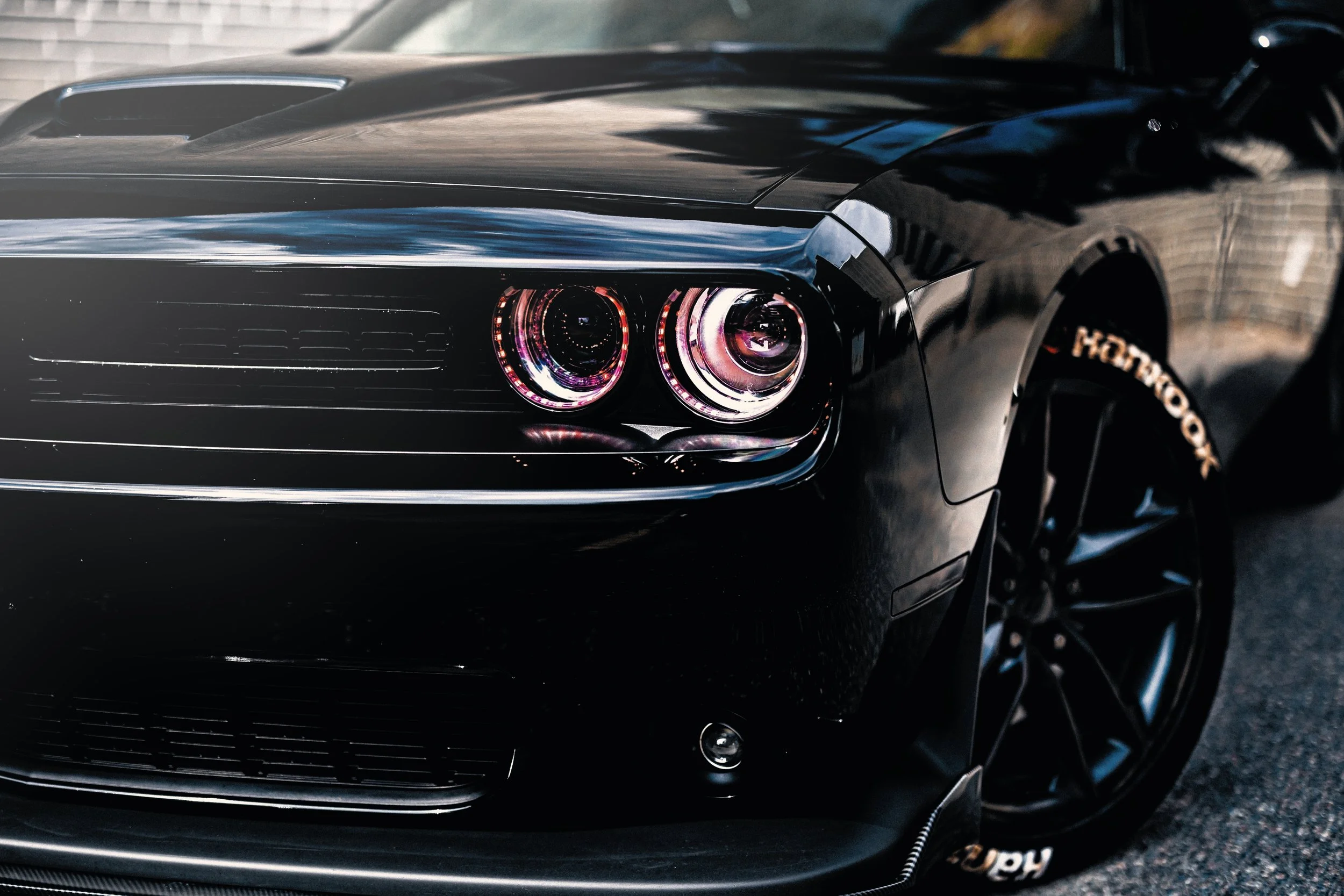 Close-up of a sleek black sports car with glowing pinkish-red headlights and a shiny surface reflecting its surroundings.