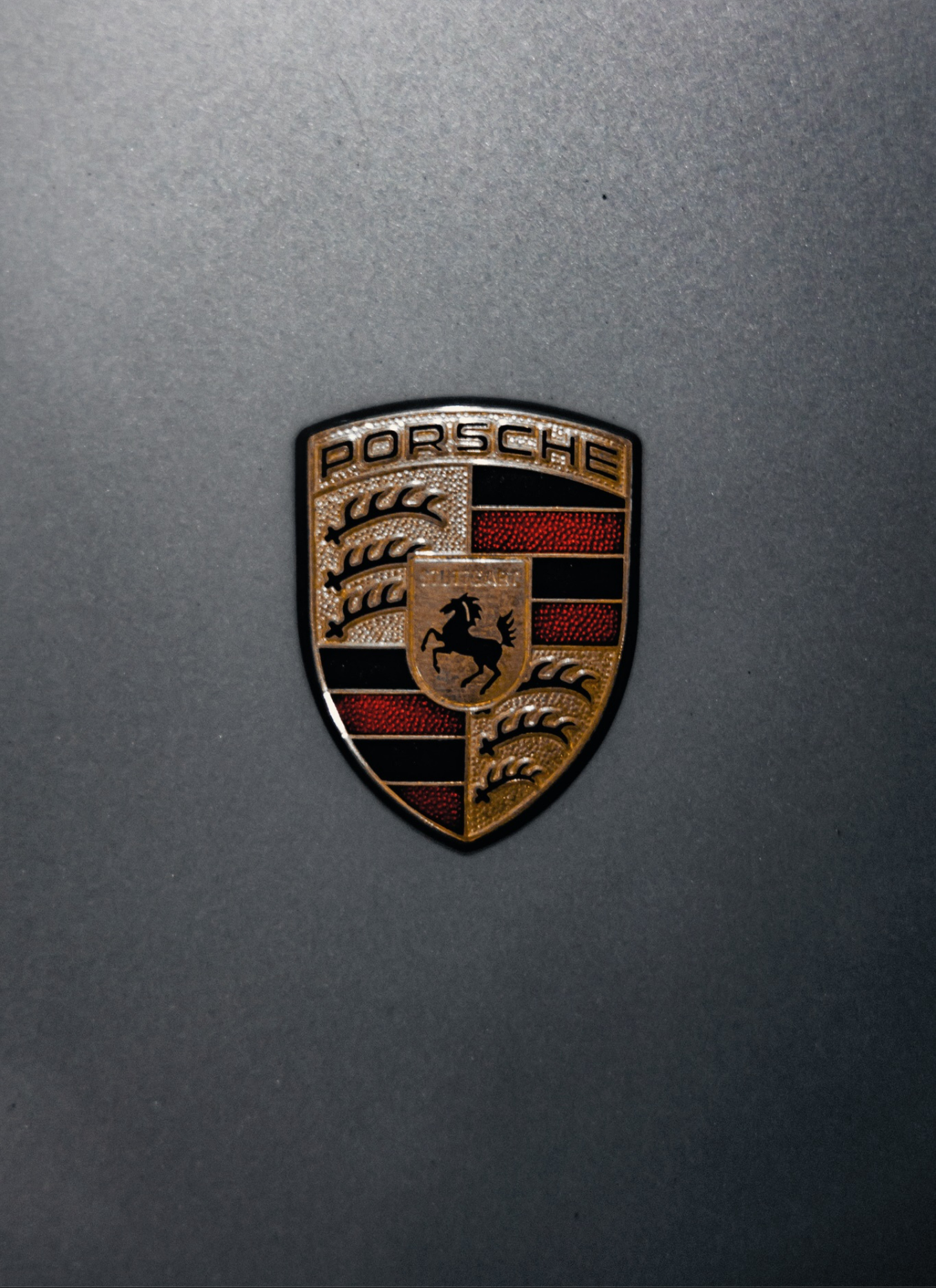 Close-up of a Porsche emblem on a metallic grey surface.