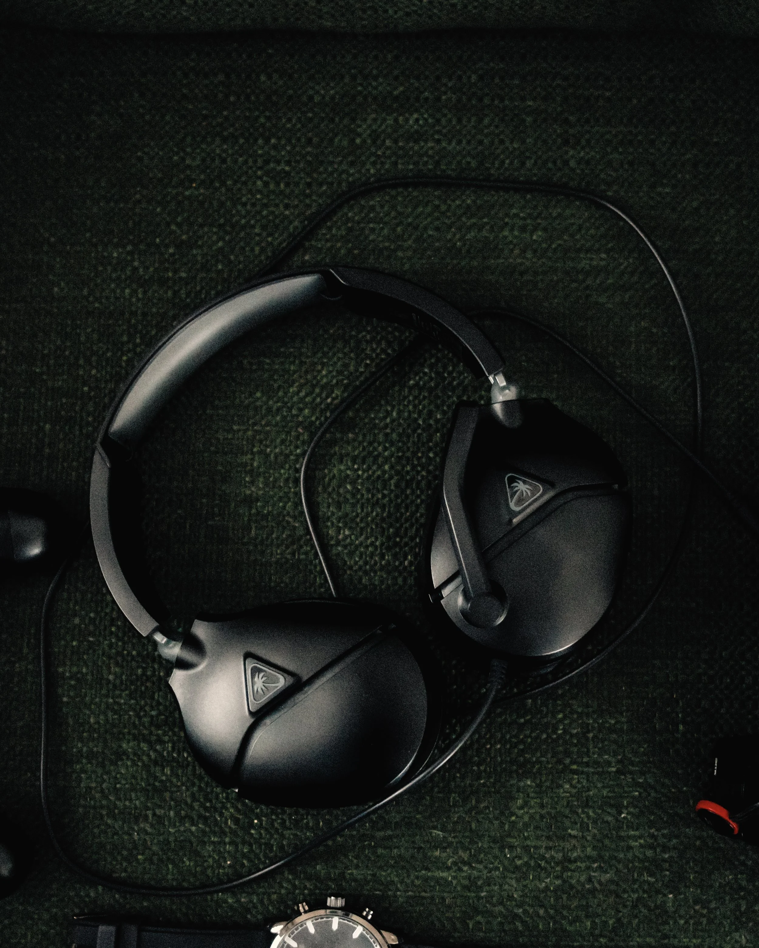 Overhead view of a pair of black and silver noise-canceling headphones and a black wristwatch on a dark textured surface.