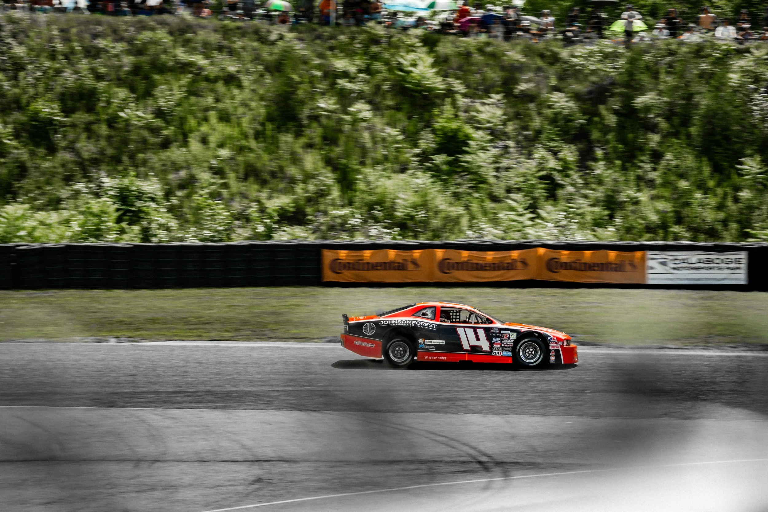 A race car speeding on a track with a crowd of spectators watching from the stands in the background.