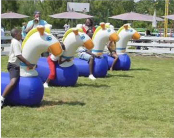 Children riding inflatable zebra-shaped rides at an outdoor amusement park.
