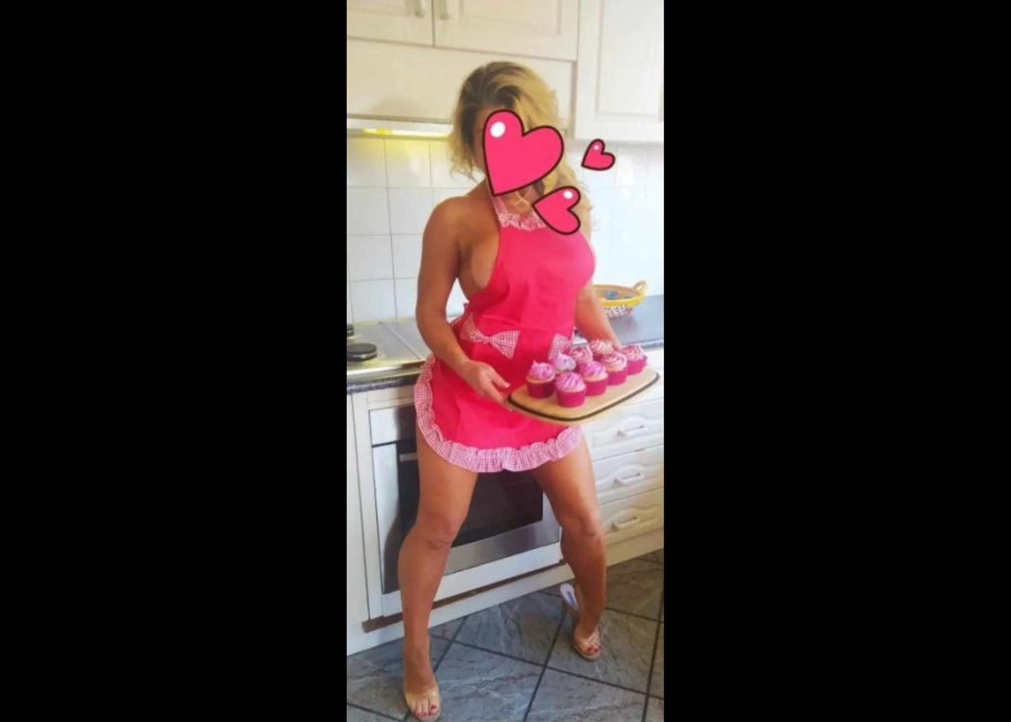 Woman in a pink apron holding a tray of cupcakes in a kitchen
