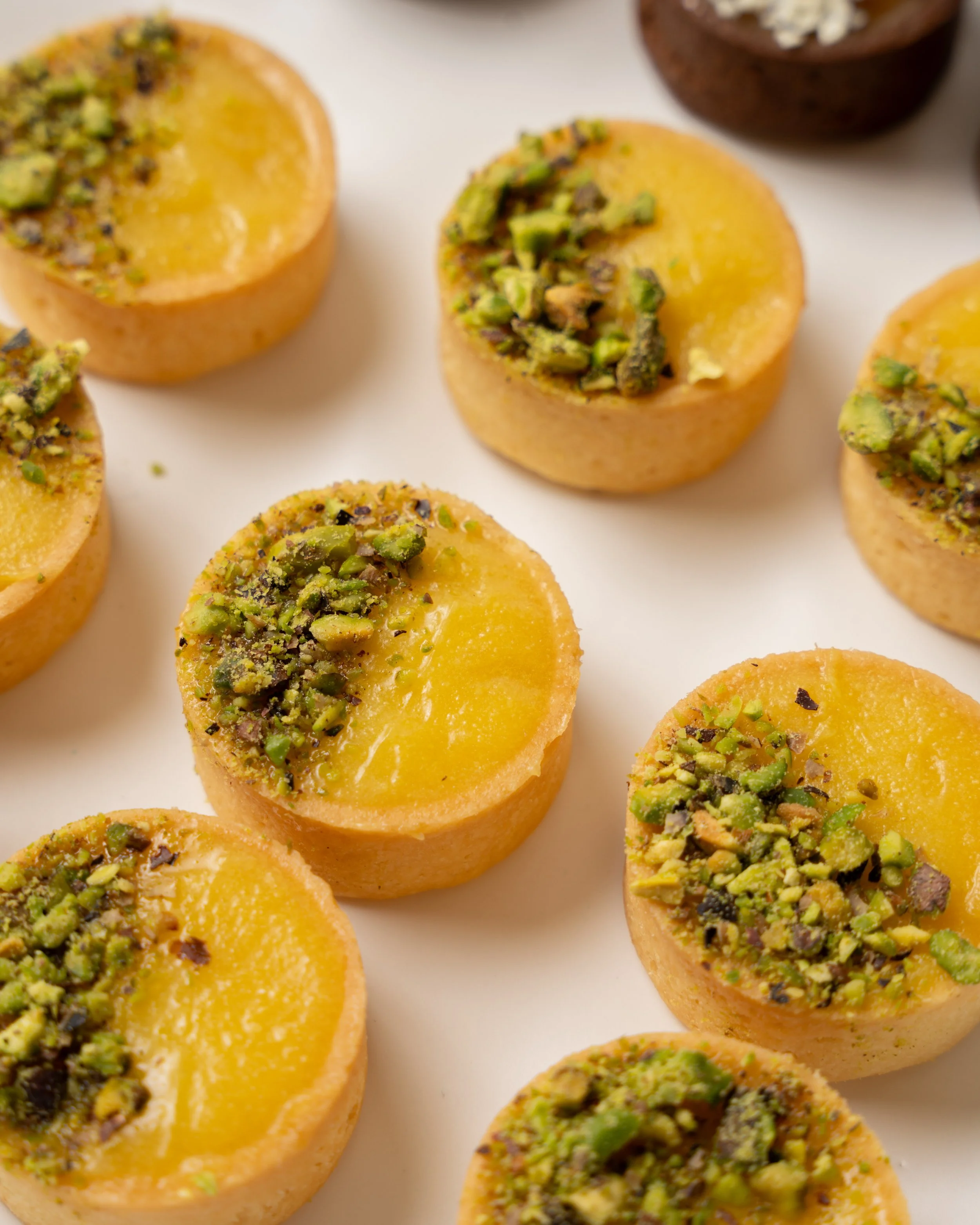 Close-up of multiple pistachio baklava pieces topped with crushed pistachios on a white surface.