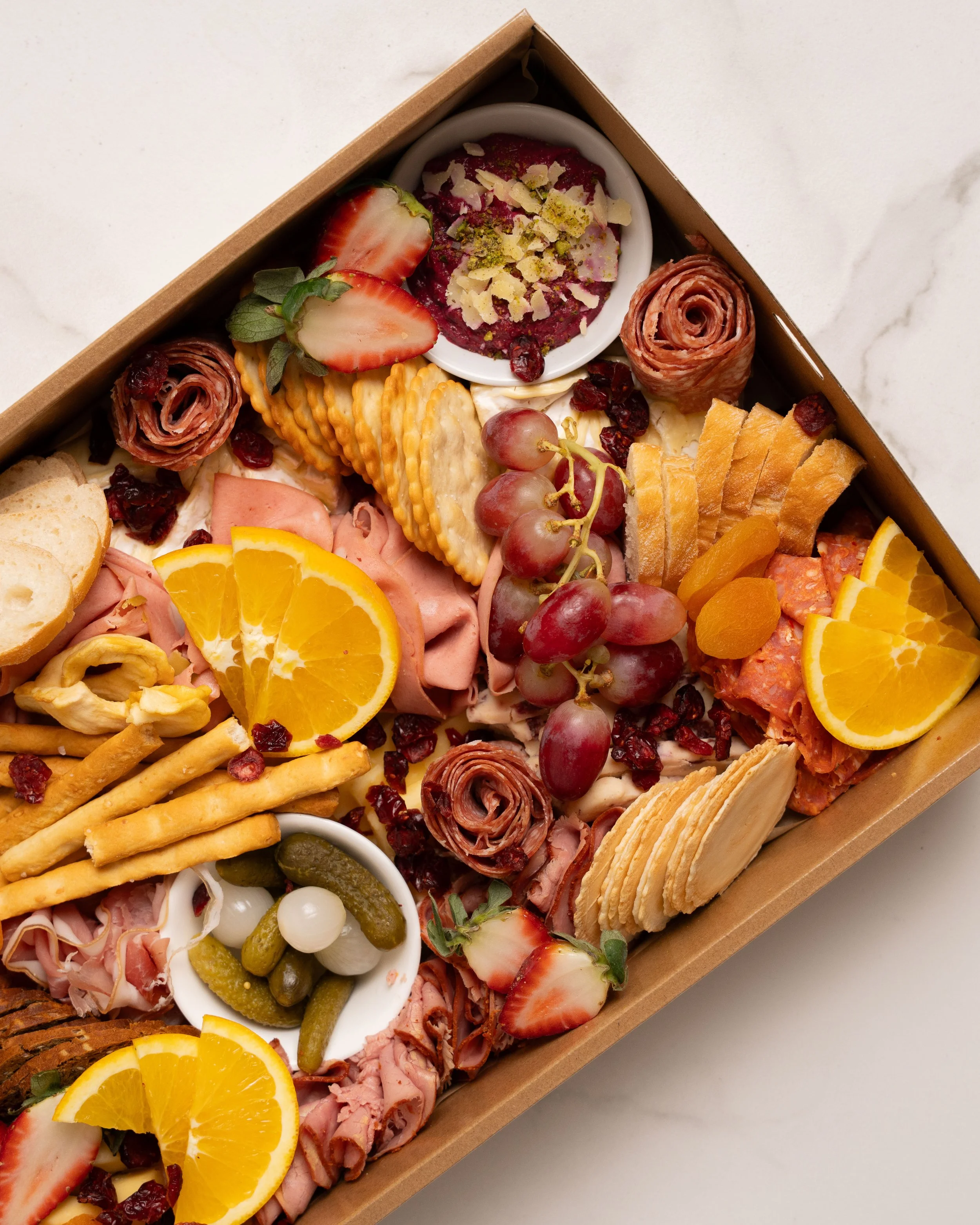 Assorted charcuterie board with strawberries, grapes, orange slices, cheese, crackers, meats, olives, and dip.