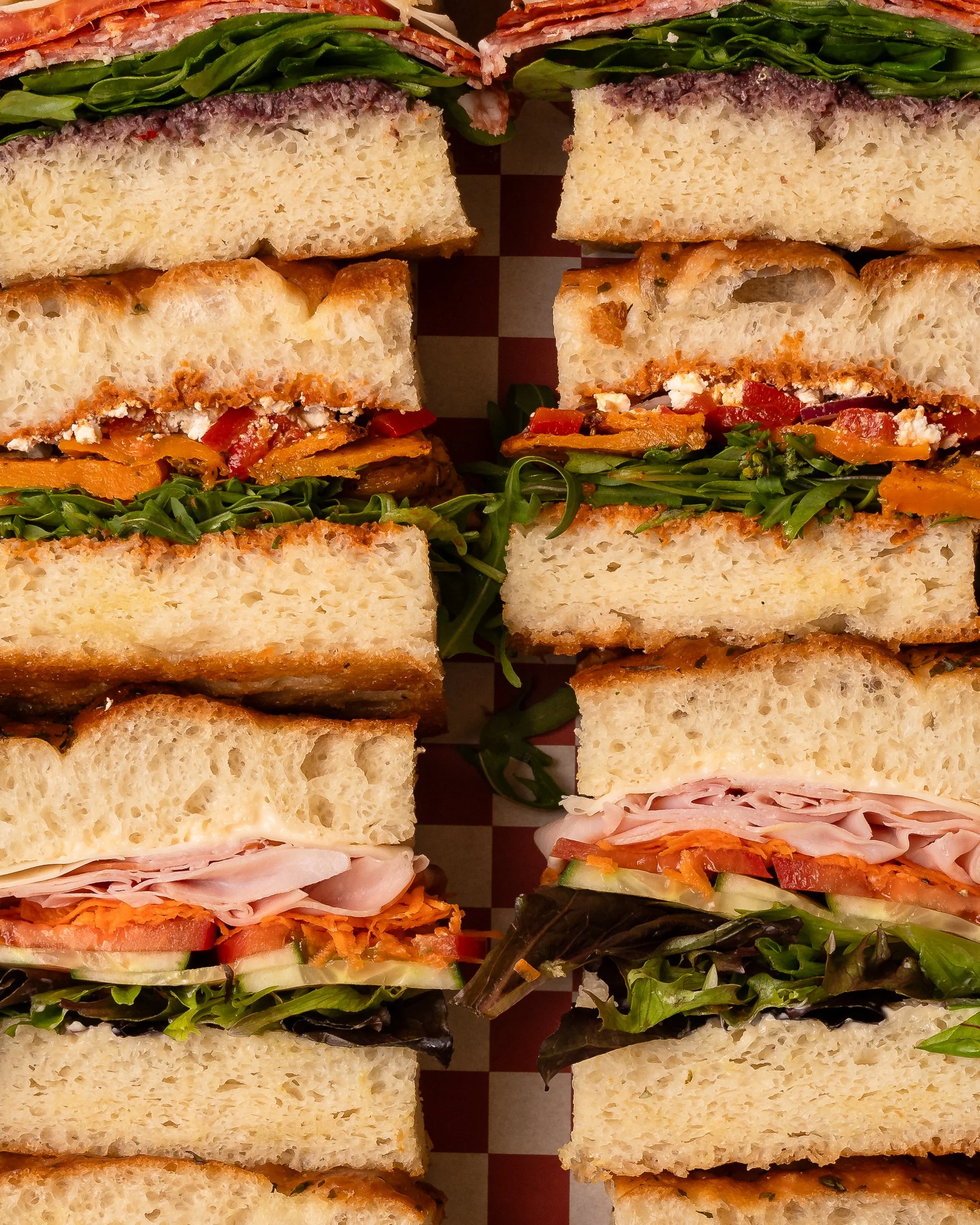 Various sandwiches with different types of bread, meats, cheeses, and vegetables arranged on a tray.