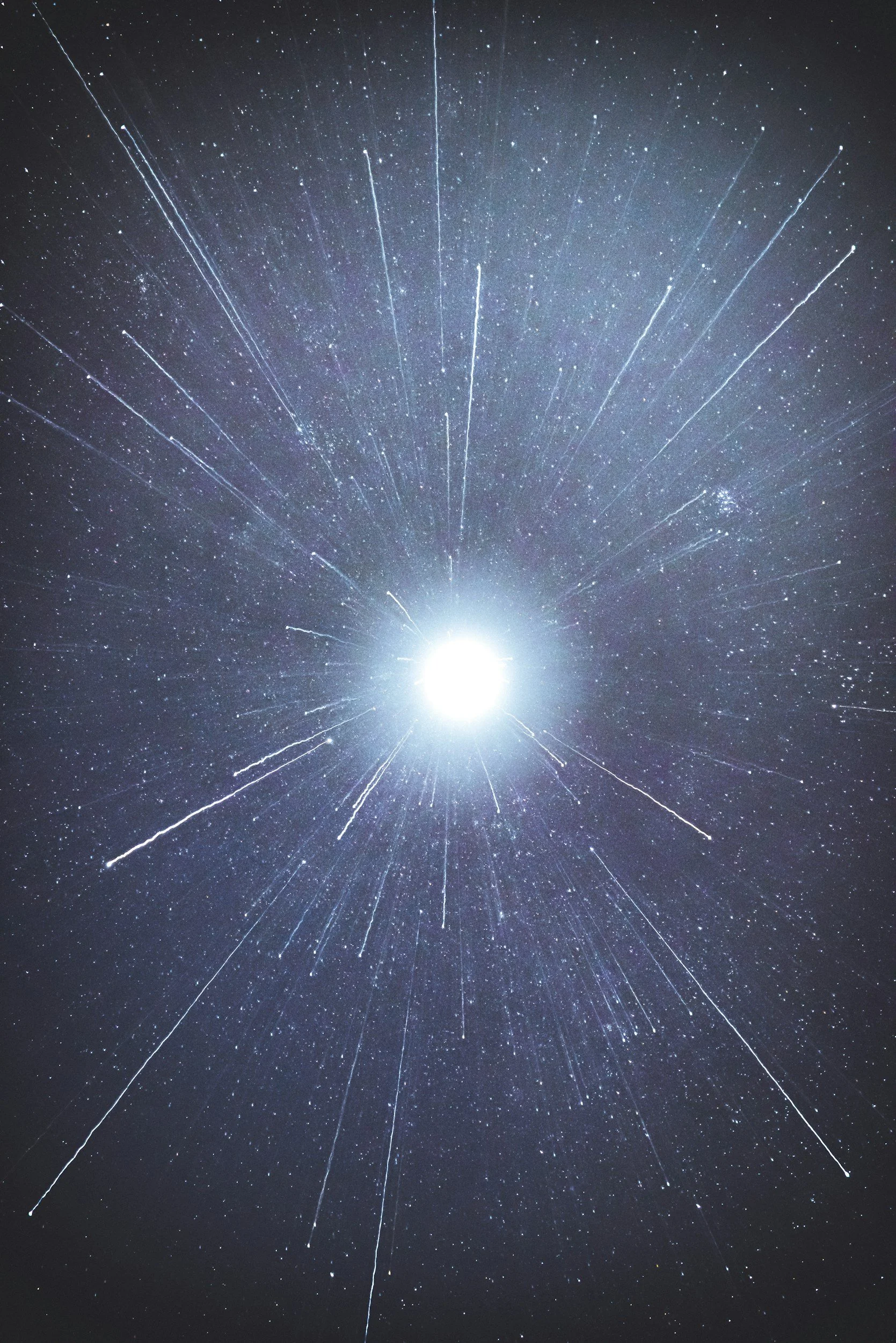 Night sky with a bright object and streaks of light radiating outward, resembling a meteor shower or shooting stars.