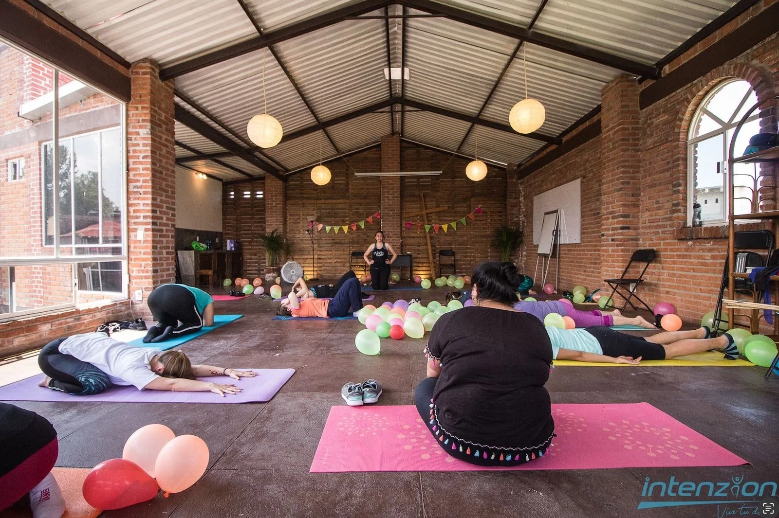 Cynthia Ramírez leading an indoor yoga class with participants in a stretching pose.