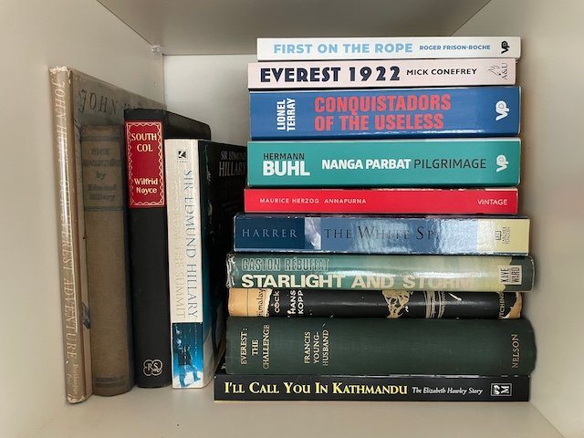 a bookshelf containing a large stack of books about early mountaineering expeditions