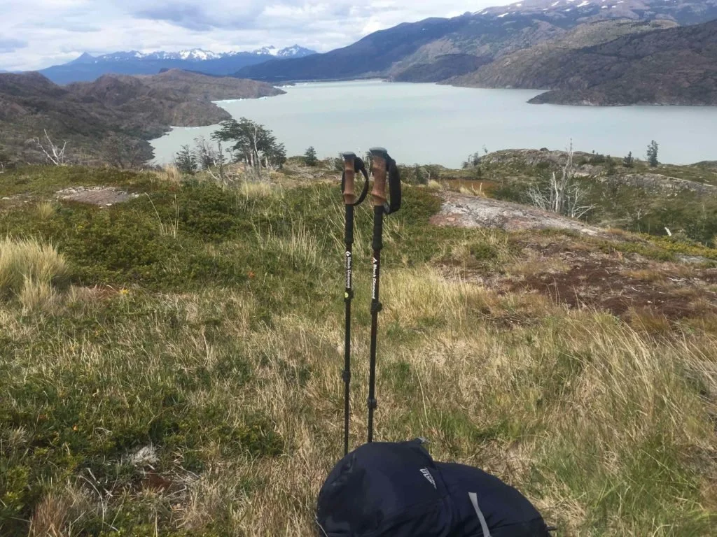 hiking poles and pack at a rest stop on grassy ground with view over lake towards a glacier
