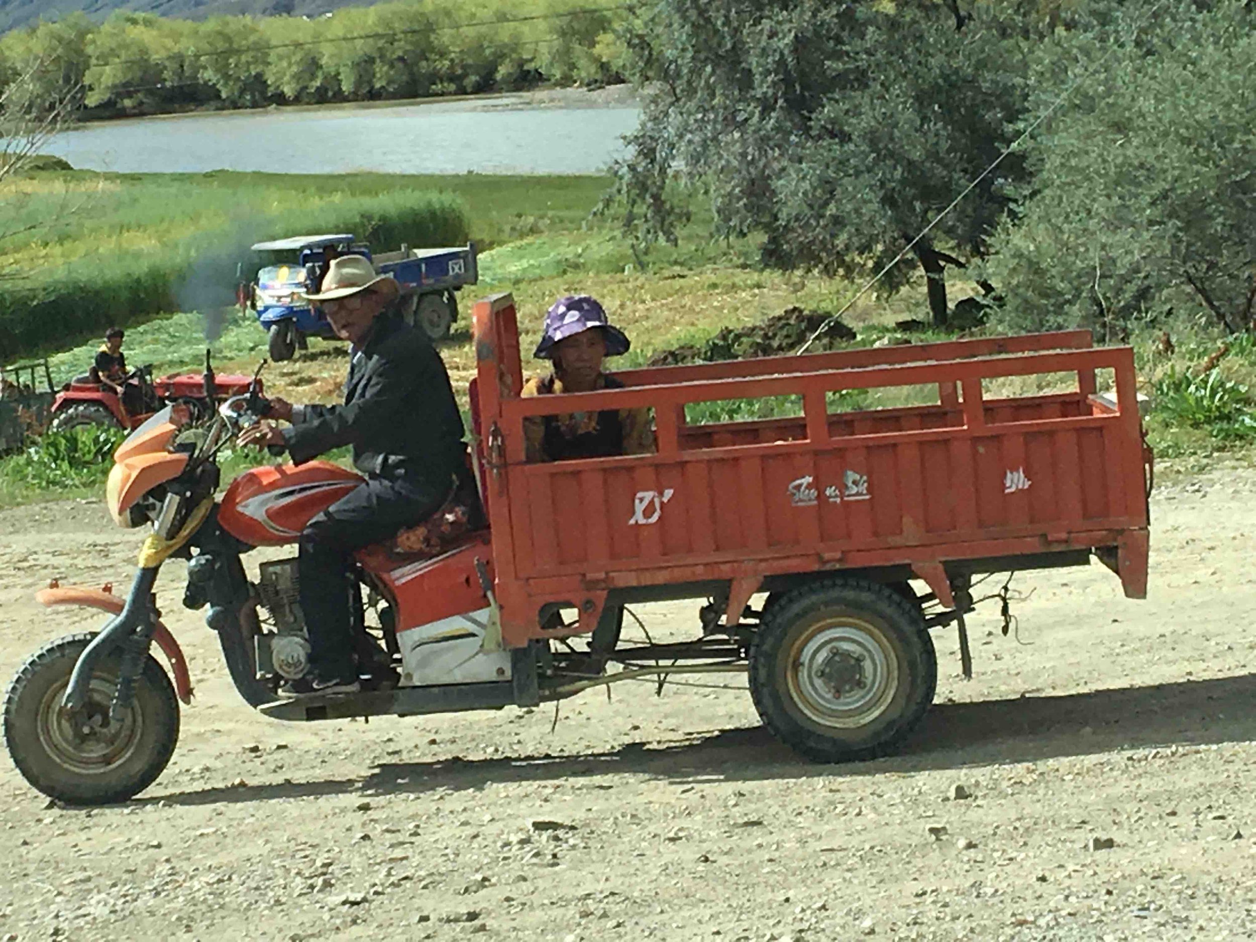 a man driving 3-wheeled vehicle with a person sitting in the back