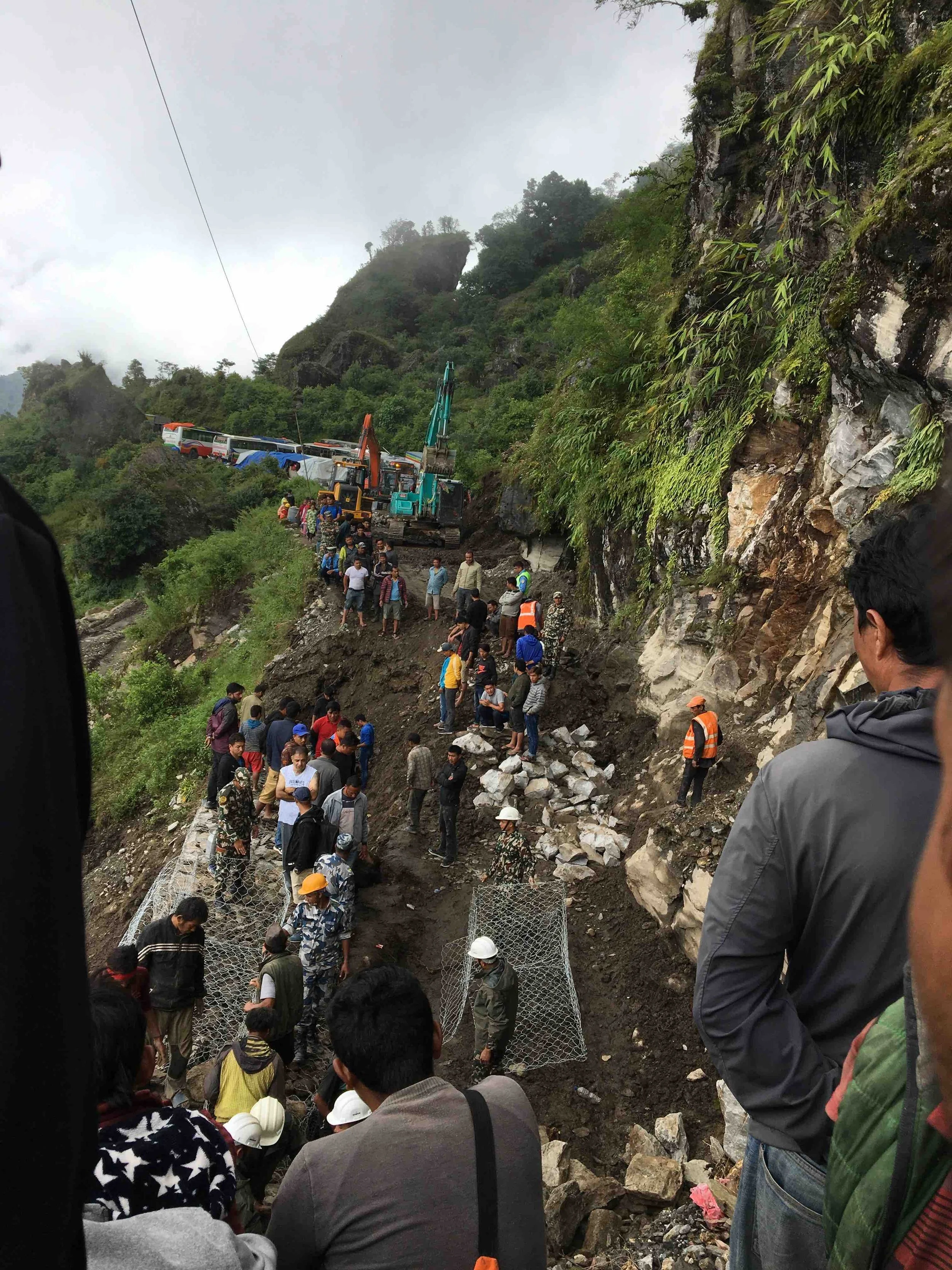 Landslide on the road with diggers repairing it and people and vehicles waiting either side