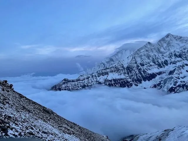 view from above the clouds looking across at mountains in dusky light after sunset