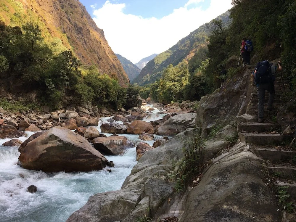 a trekker going up steps alongside a fast-flowing rocky river