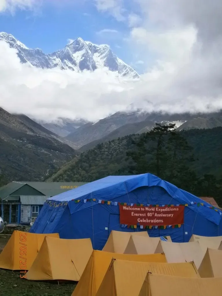 dining and camping tents pitched in front of Himalayan peaks with a sign for the 60th anniversary celebrations