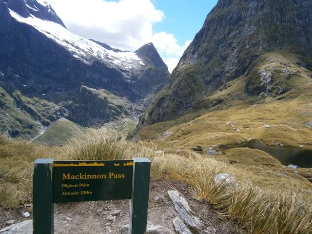 signpost at the top of Mackinnon Pass on the Milford Track n New Zealand with mountain backdrop