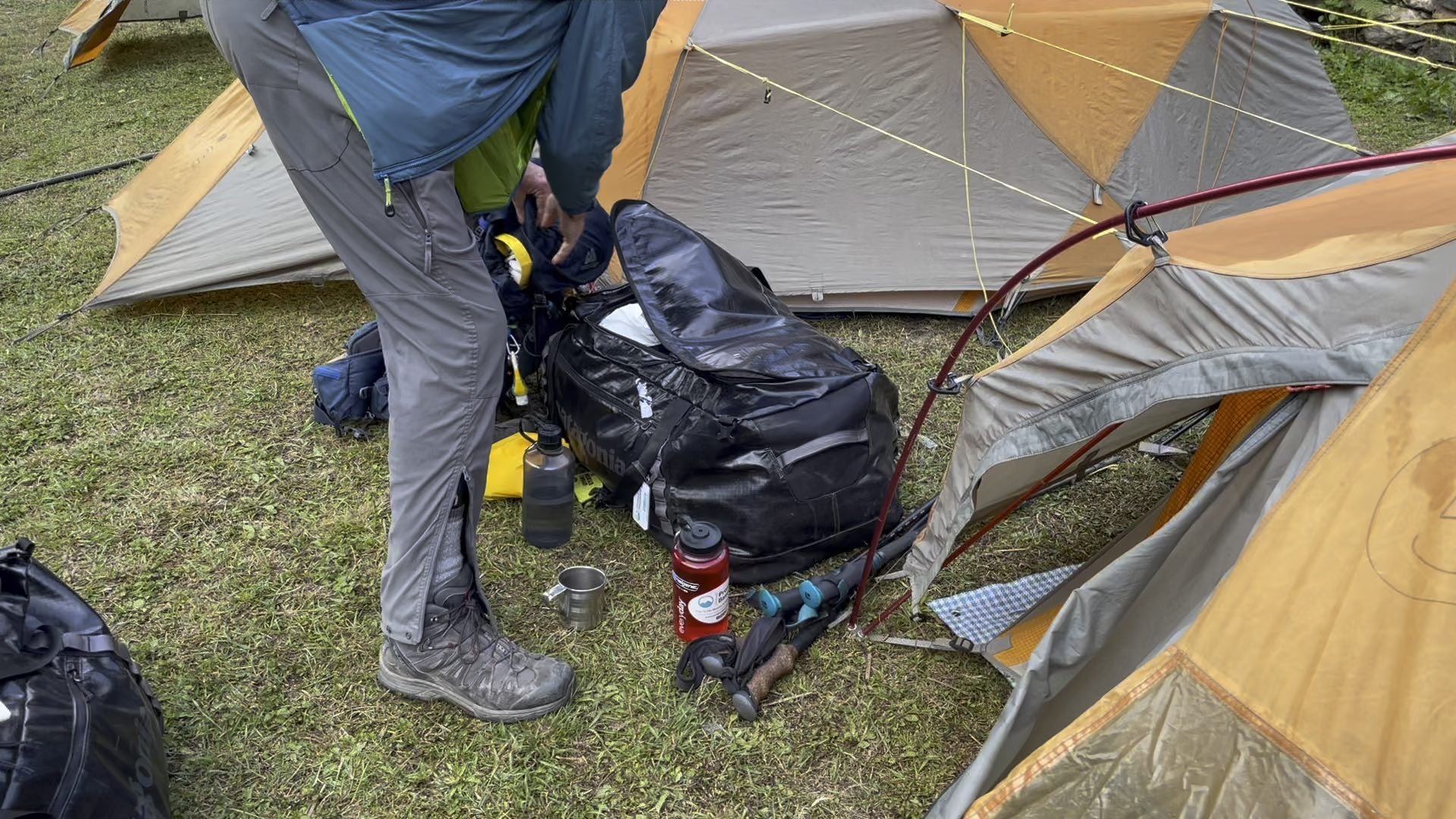 a trekker packing their kitbag next to a tent