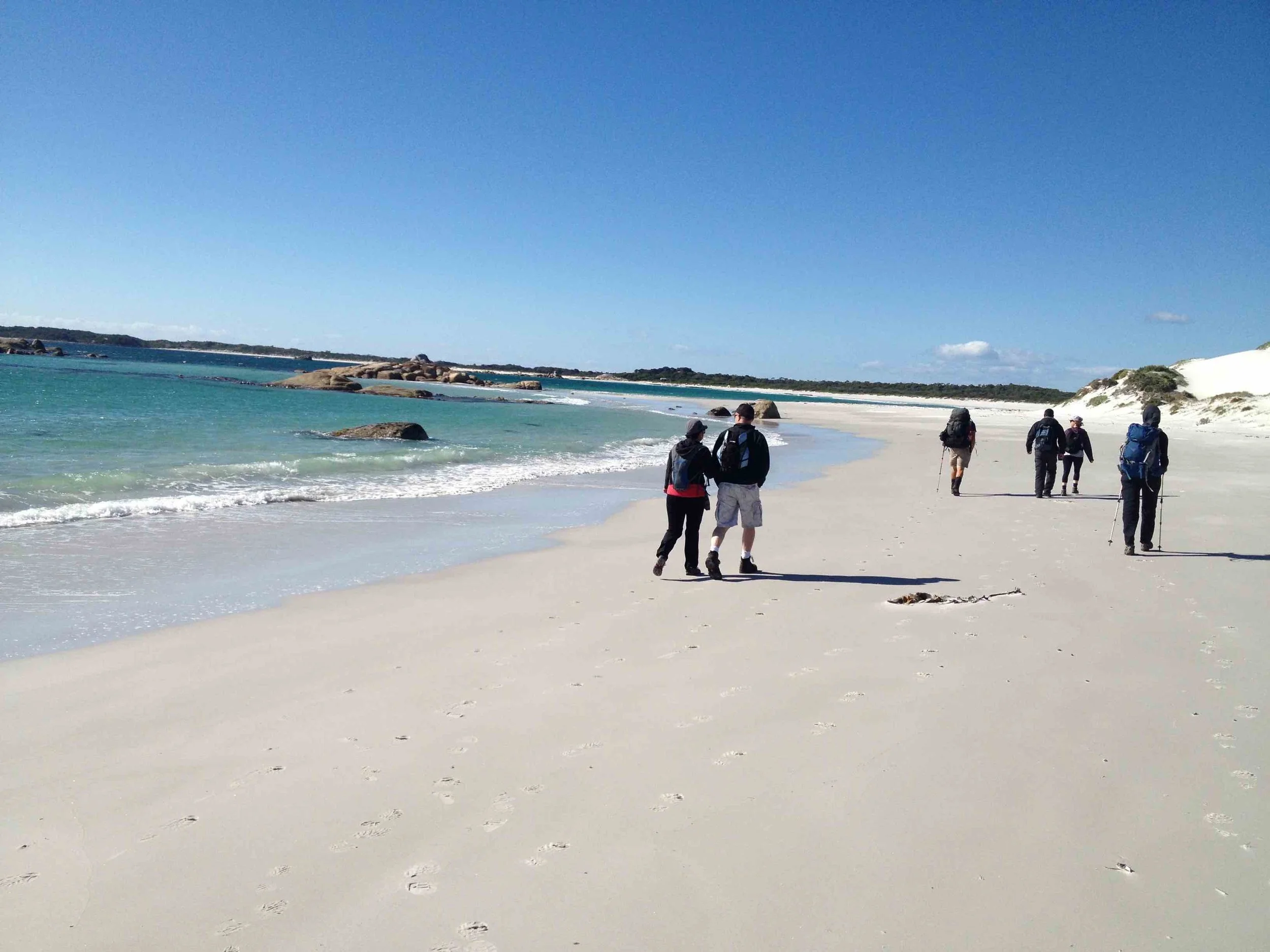 hikers walking along white sand beaches