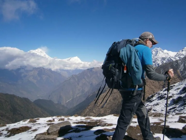 a trekker walking along snow and rock with Himalayan mountain view in the distance