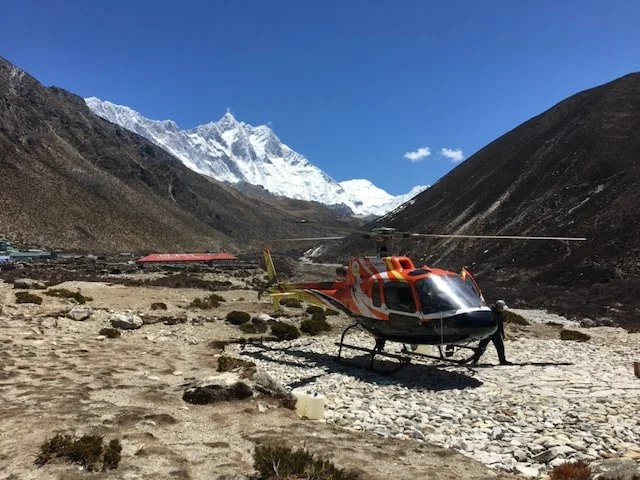 helicopter on a rocky landing pad with mountains behind