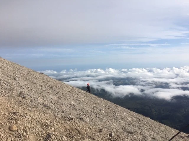 a hiker going above the clouds on the steep slope of Mt Taranaki